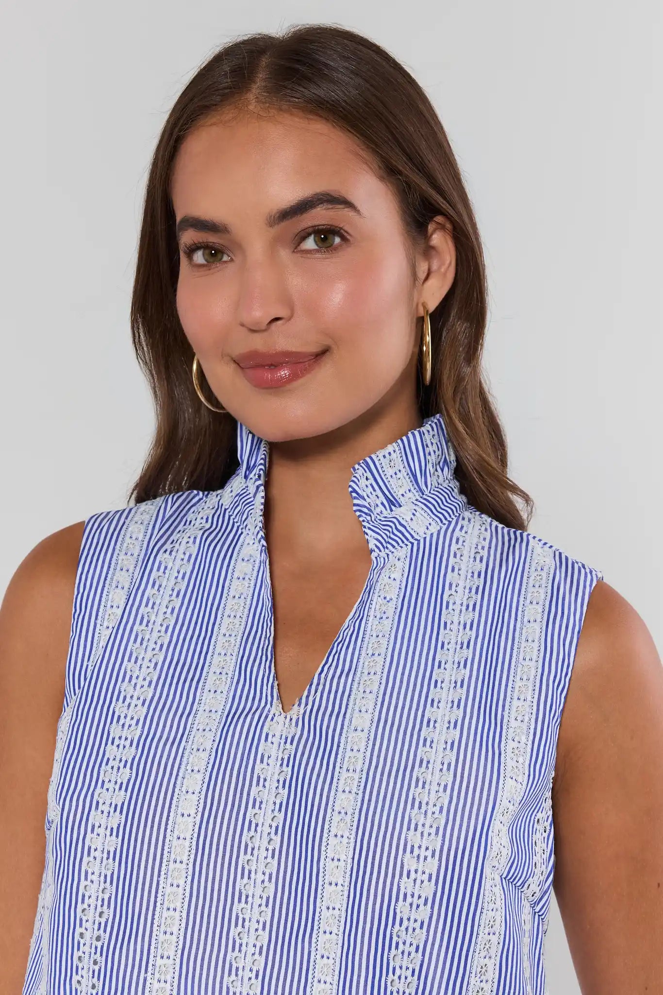 Woman wearing a blue and white striped sleeveless top with lace details on a plain background close up