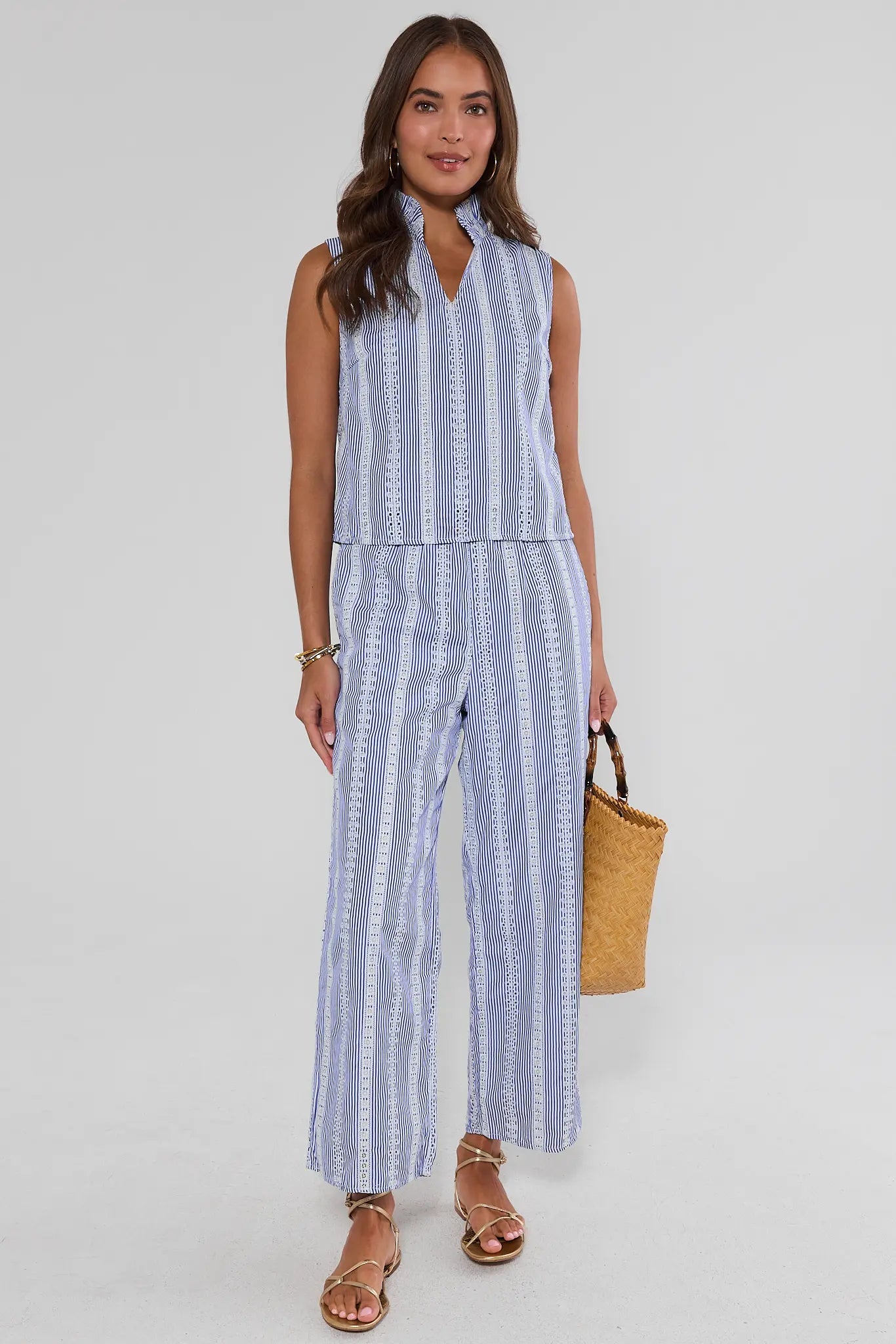 Woman wearing a blue and white striped sleeveless top and pants set, holding a woven bag on a light gray background.