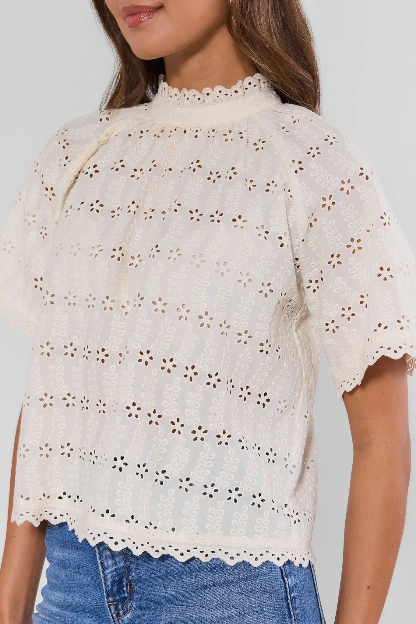 close up Woman wearing a white lace top with blue jeans on a plain background