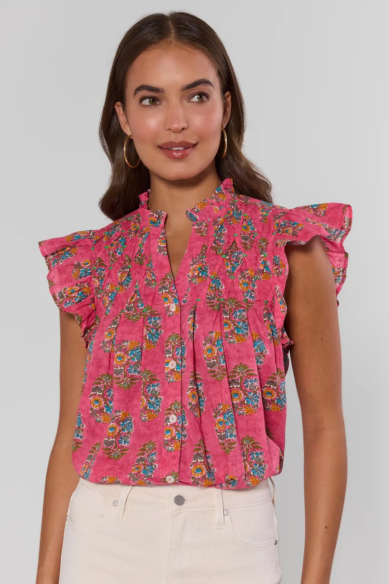 Woman wearing a pink floral blouse against a plain background standing