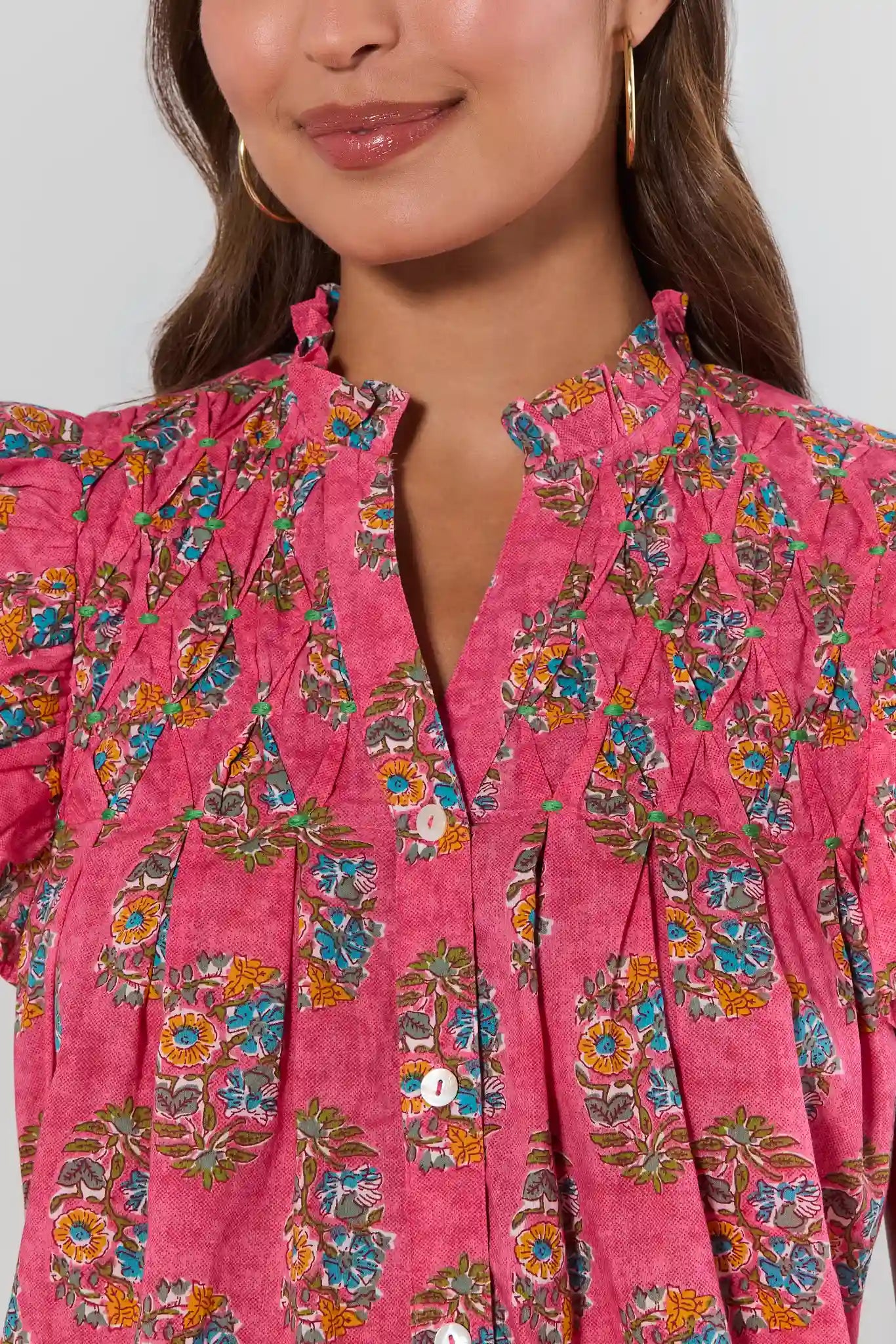 Close-up of a person wearing a pink floral blouse against a neutral background close up