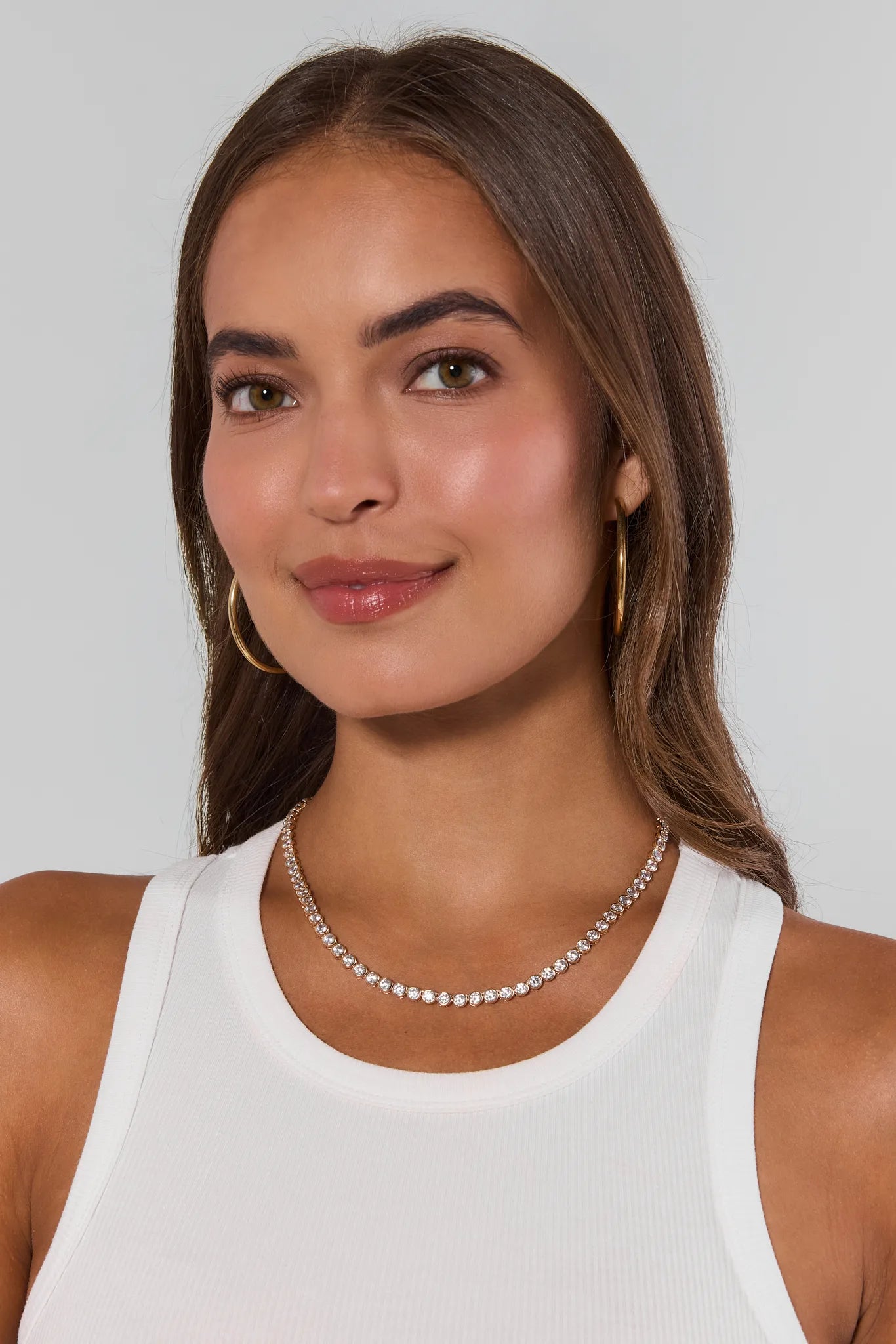 Woman wearing a white tank top and silver necklace against a plain background