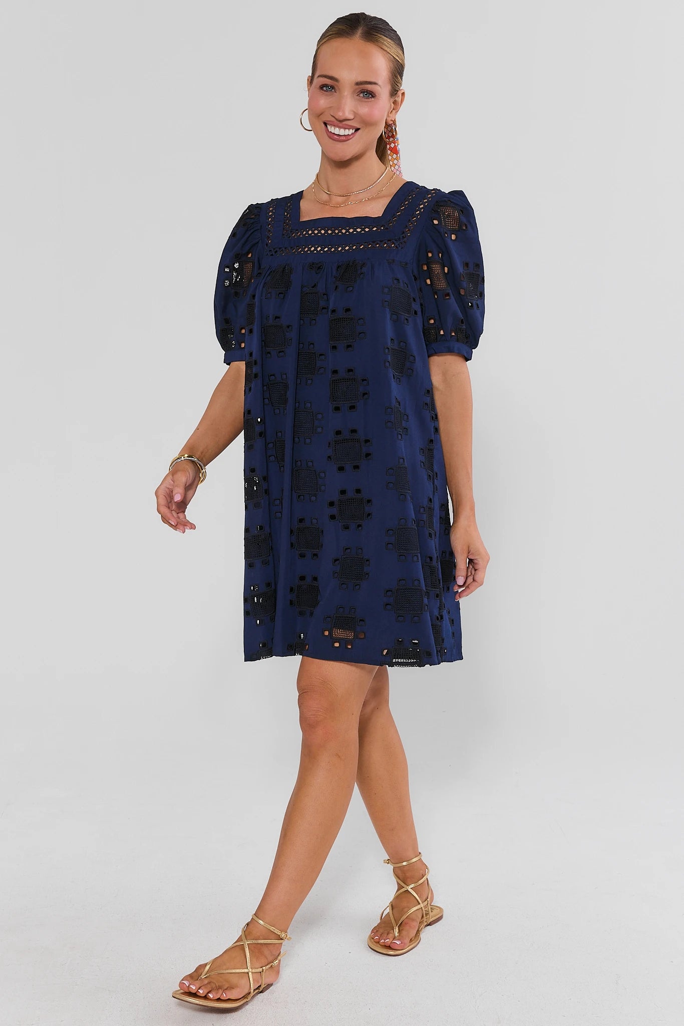 Woman wearing a navy blue dress with lace details on a white background walking