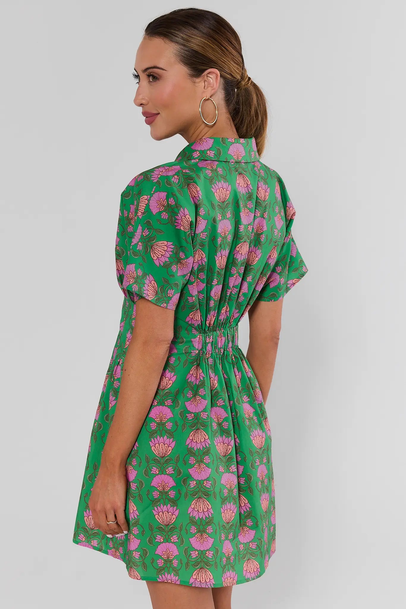 Woman standing wearing a green and pink floral olivia dress against a plain background