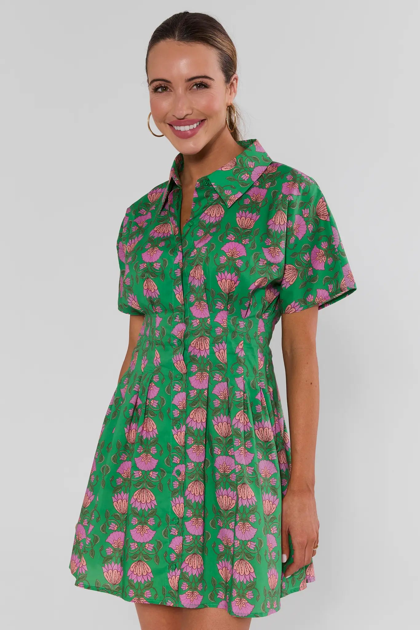 Woman wearing a green and pink patterned dress on a white background standing