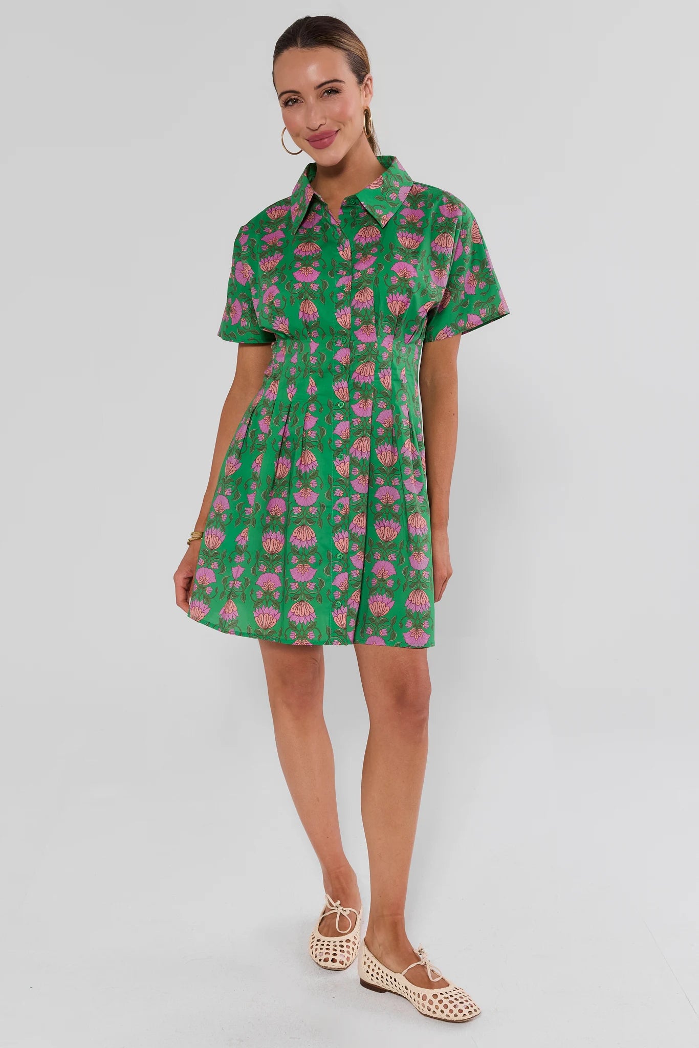 Woman wearing a green olivia dress with pink floral pattern on a plain background standing