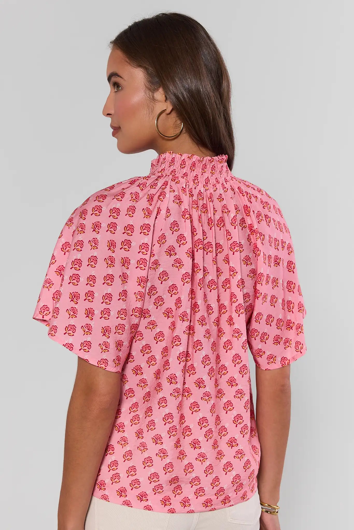 Woman wearing a pink blouse with red floral pattern on a plain background standing
