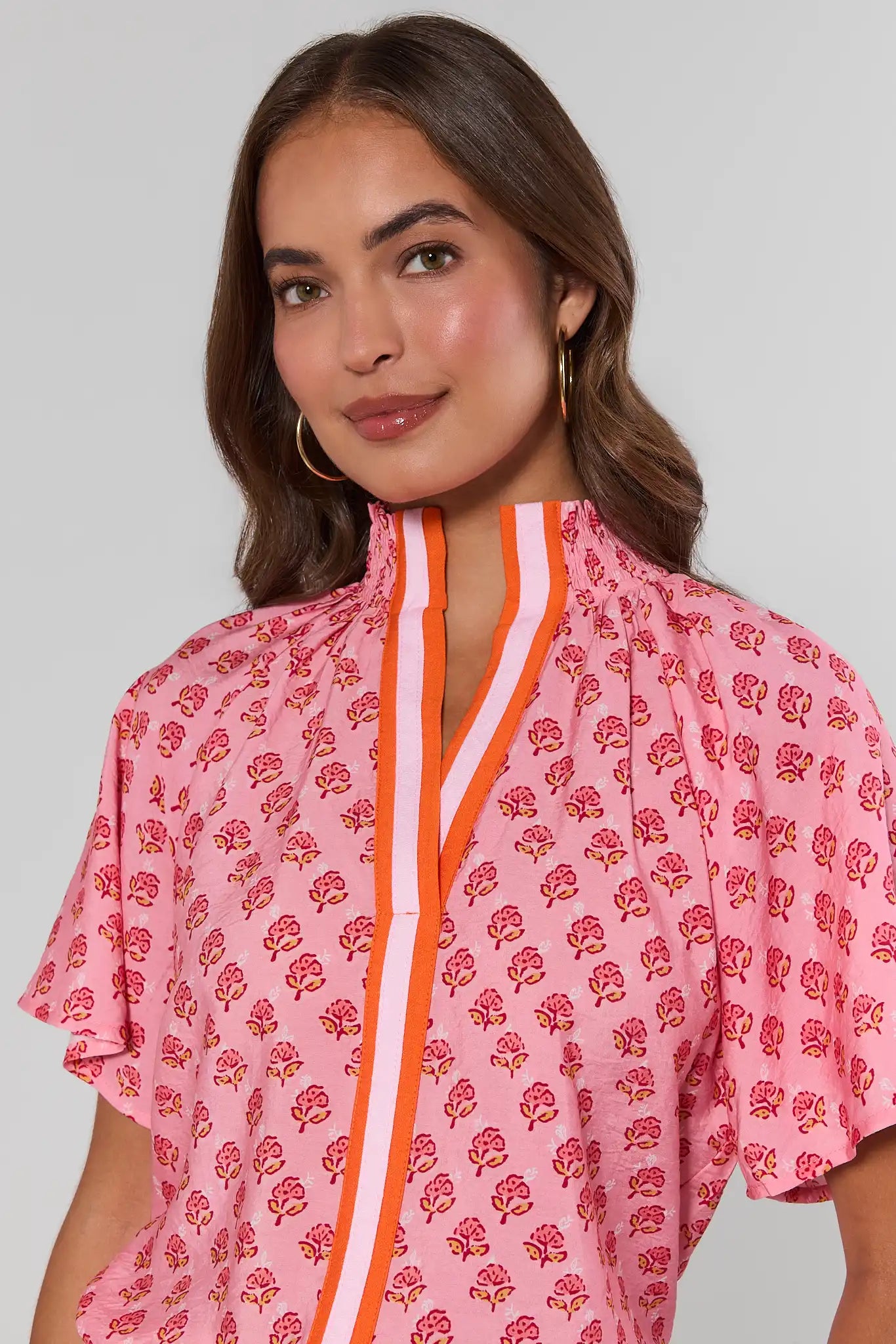 Woman wearing a pink patterned top with orange accents against a plain background close up