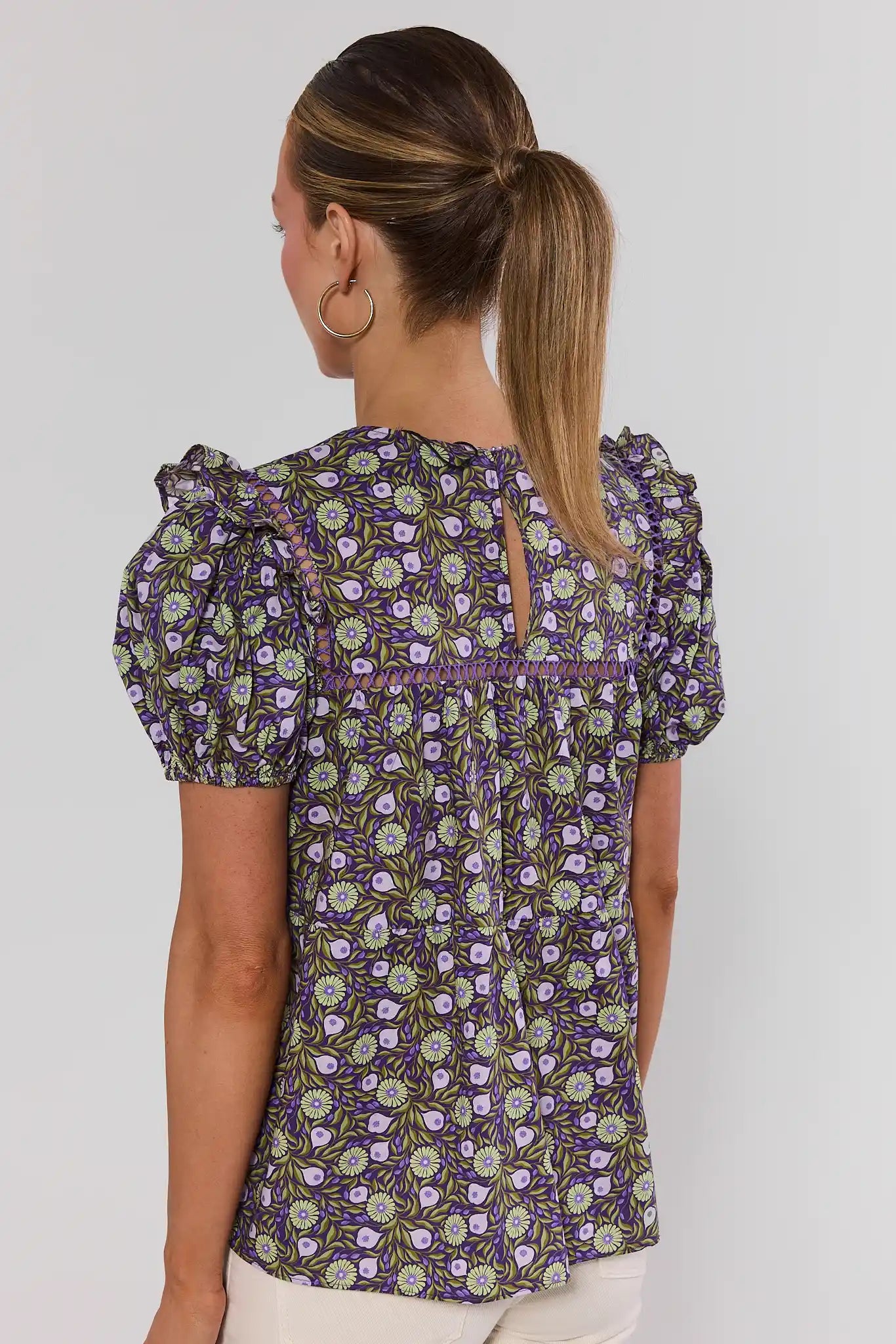Woman wearing a floral patterned blouse against a plain background standing