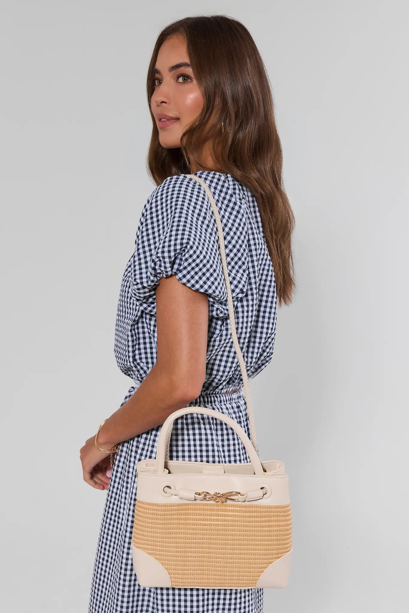 Woman holding a beige handbag against a plain background