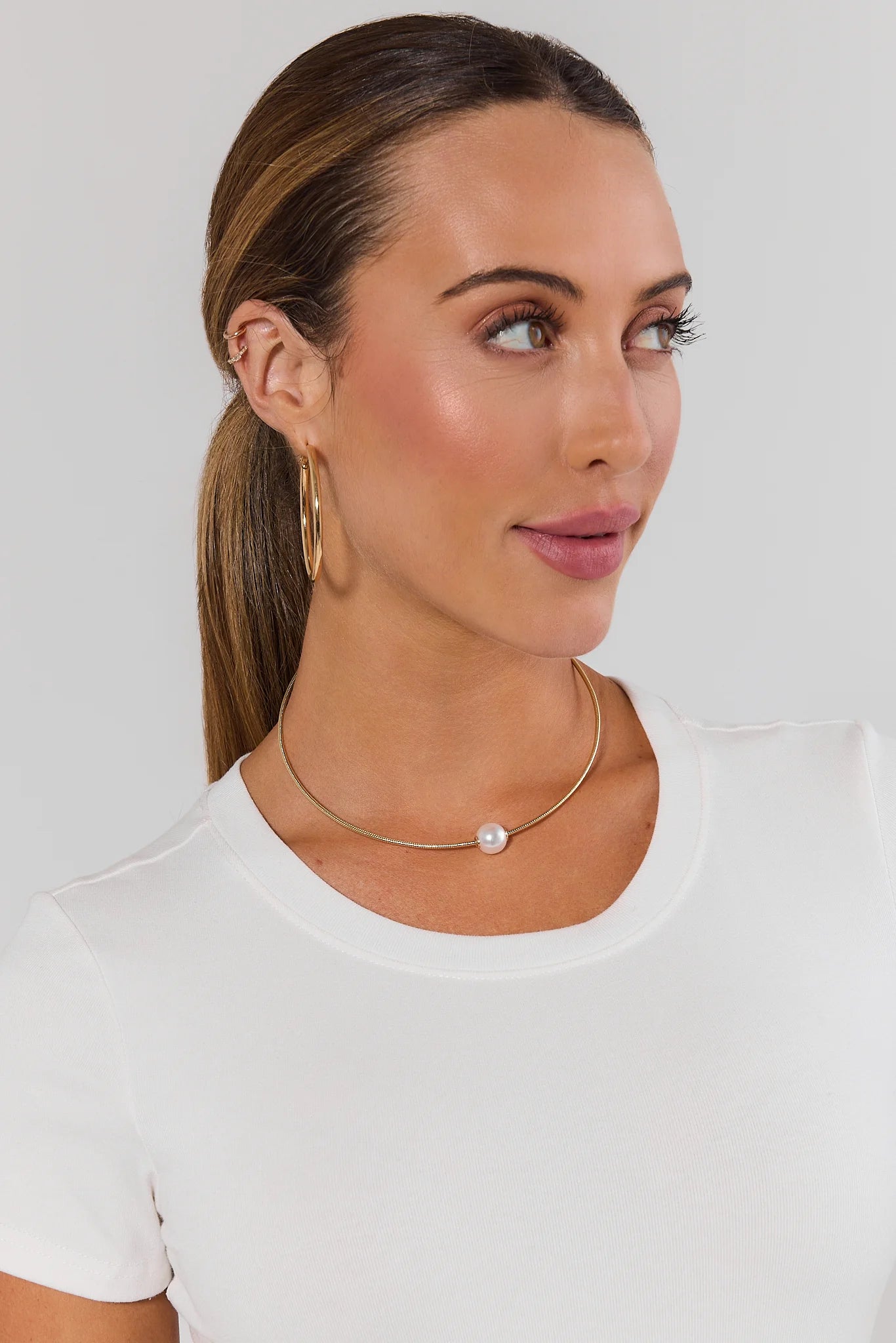 woman wearing gold pearl charm necklace on white background