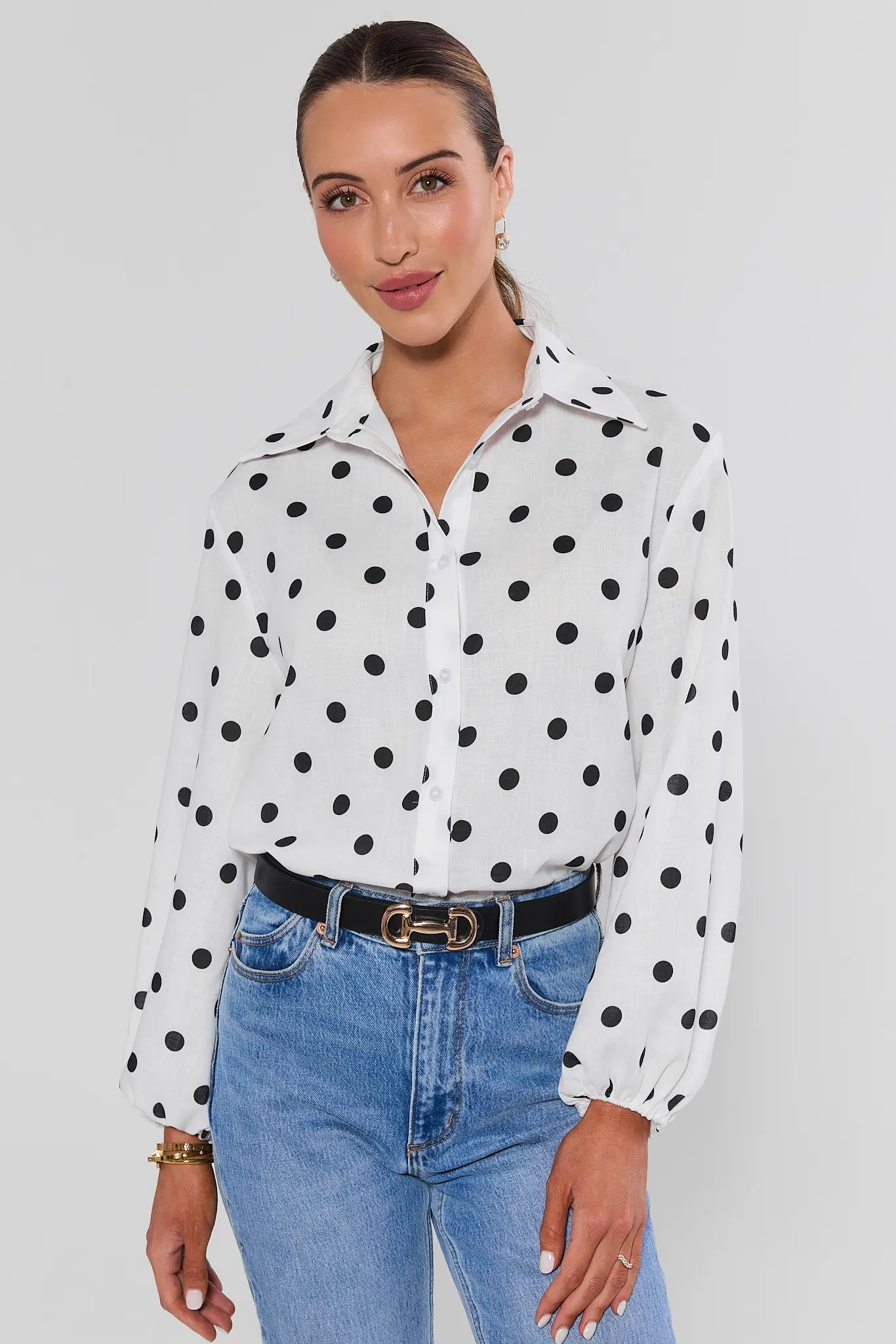 Woman wearing white polka dot top with jeans on a white background