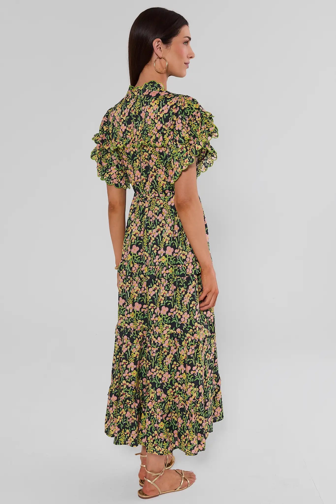 Woman standing to the side wearing a long-sleeved, V-neck maxi dress with a green, yellow, and pink floral print, against a plain light background.