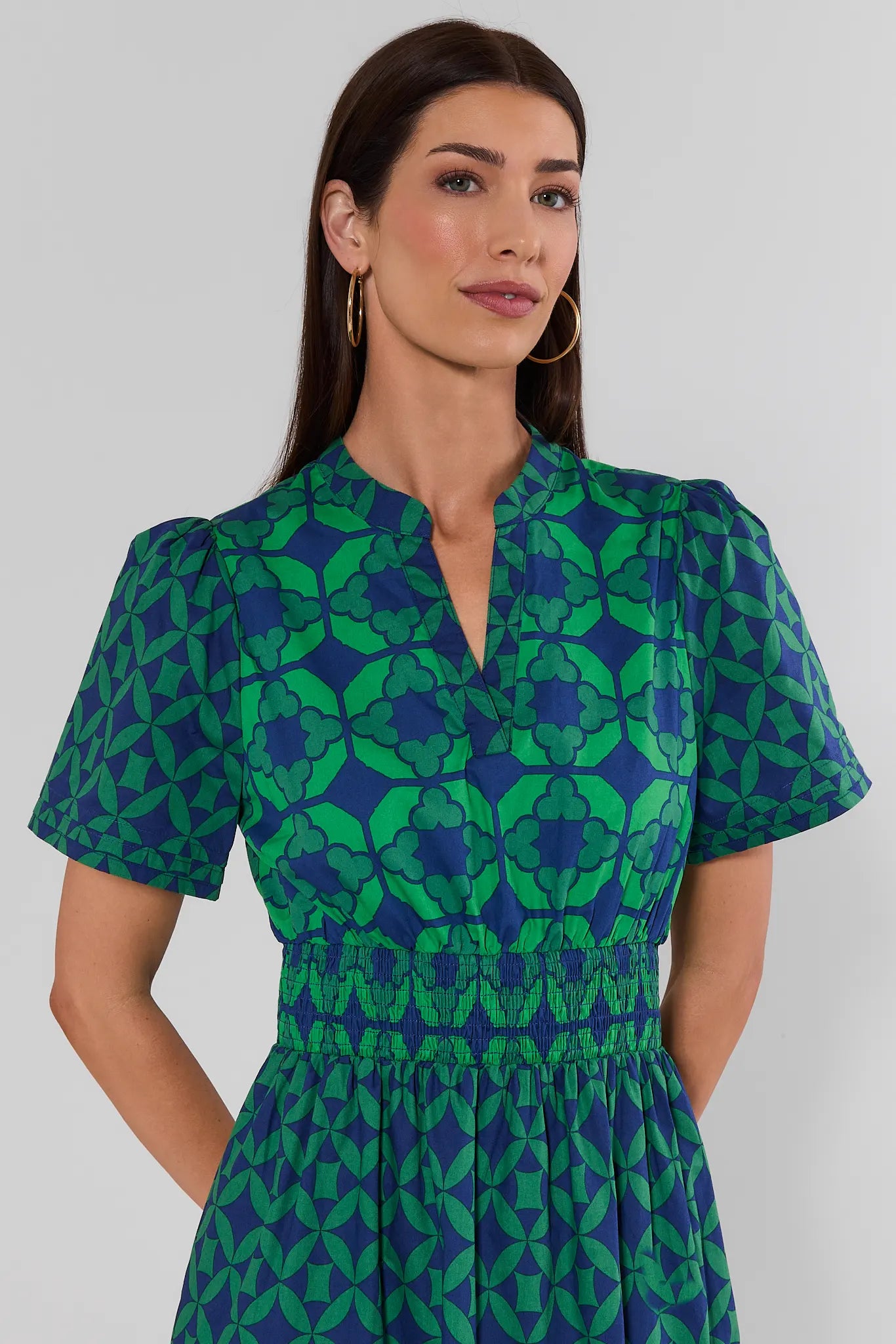 close up A woman wearing a green and blue patterned maxi dress with short sleeves and a smocked waist, on a white background