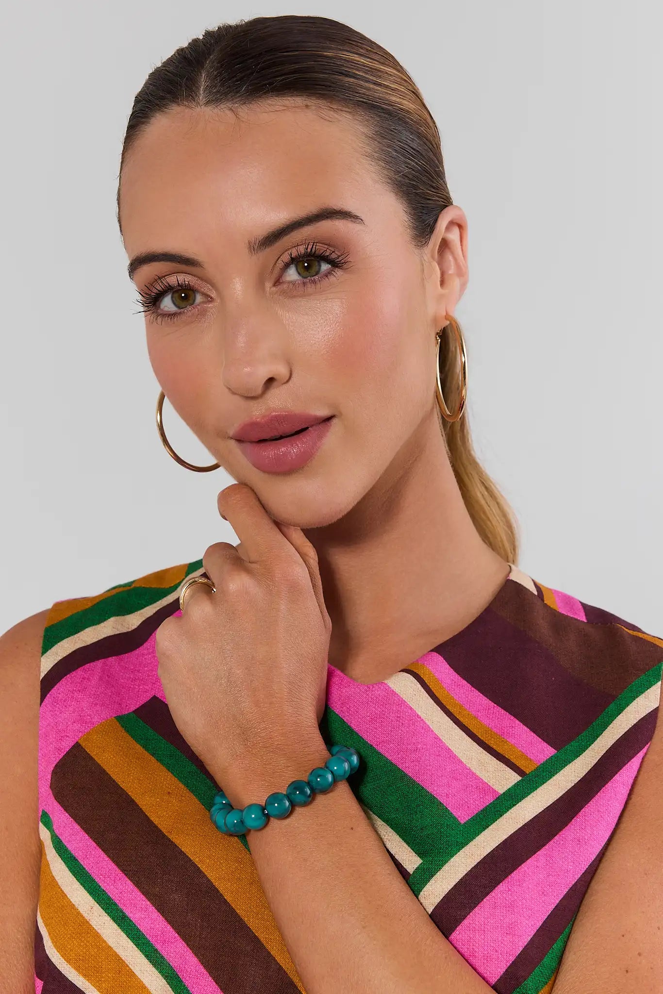 Woman wearing multi colored top with a Green Stone Stretch Bracelet on a white background