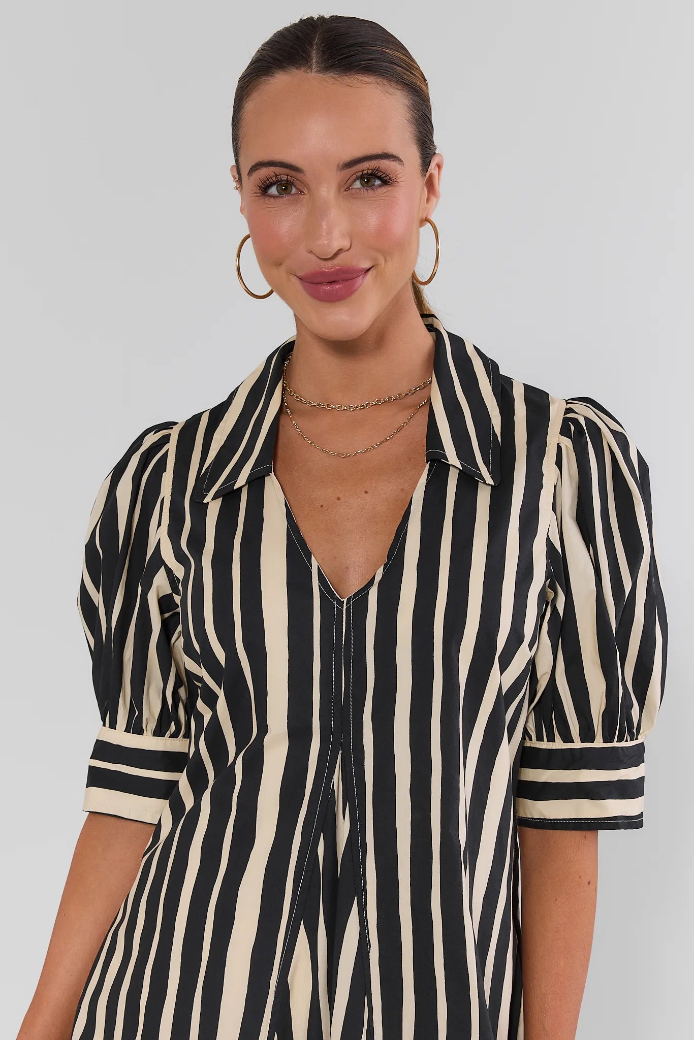 Close up of woman wearing a beige and black vertically striped midi shirt dress with short sleeves, on a white background