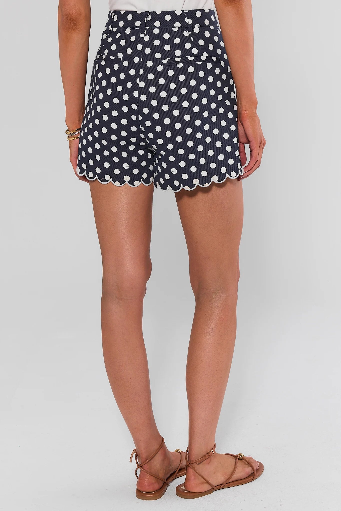 A woman standing wearing navy blue shorts with white polka dots and scalloped hems, against a light background.