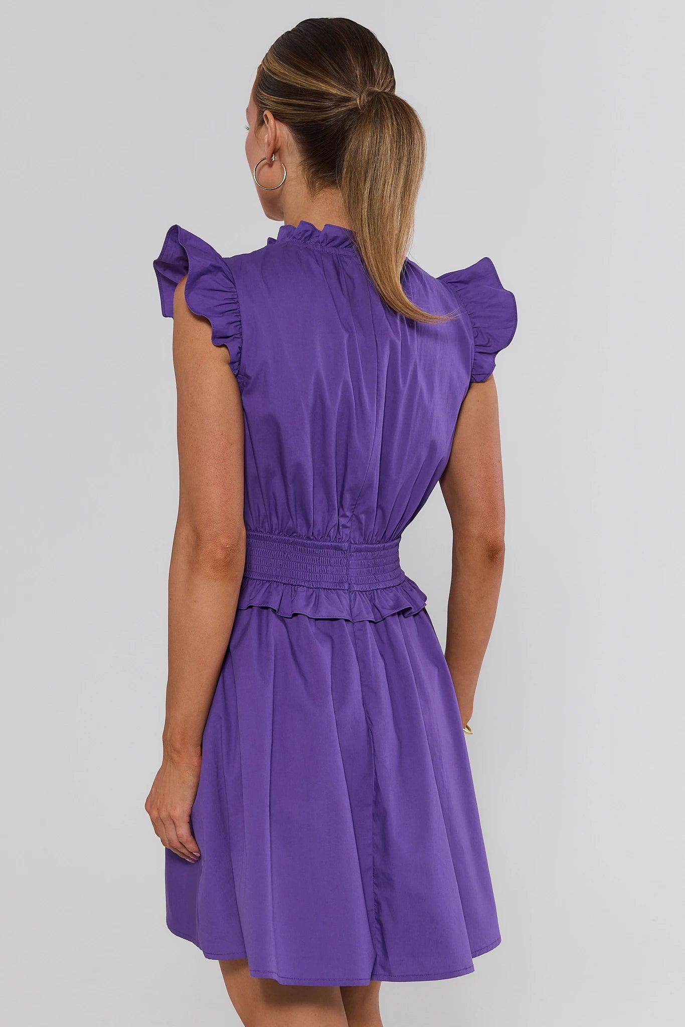 woman wearing Makayla Purple Flutter Sleeve Short Dress on a white background standing backwards