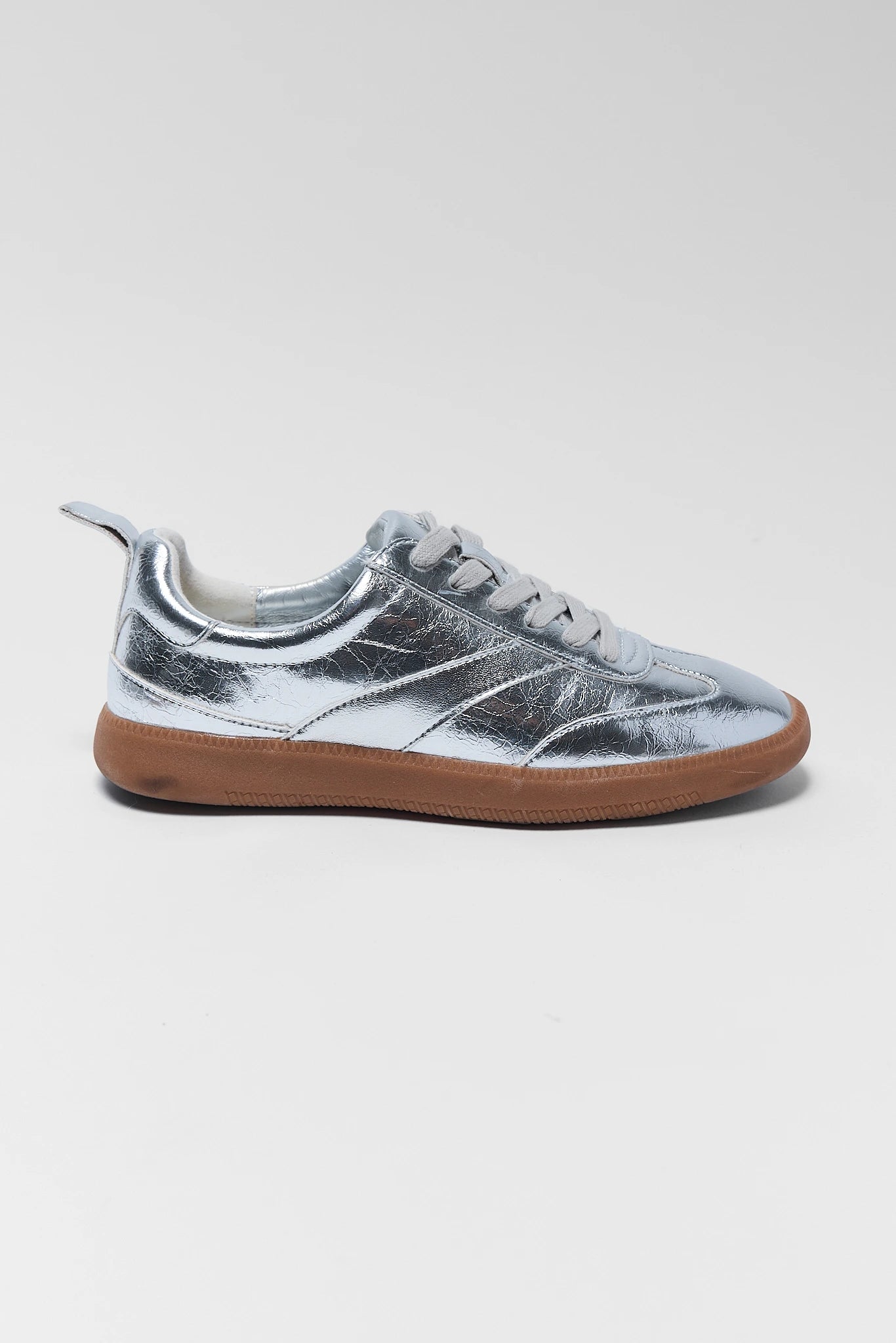 A metallic silver low-top sneaker with a gum brown sole, shown from a side profile view against a light background.