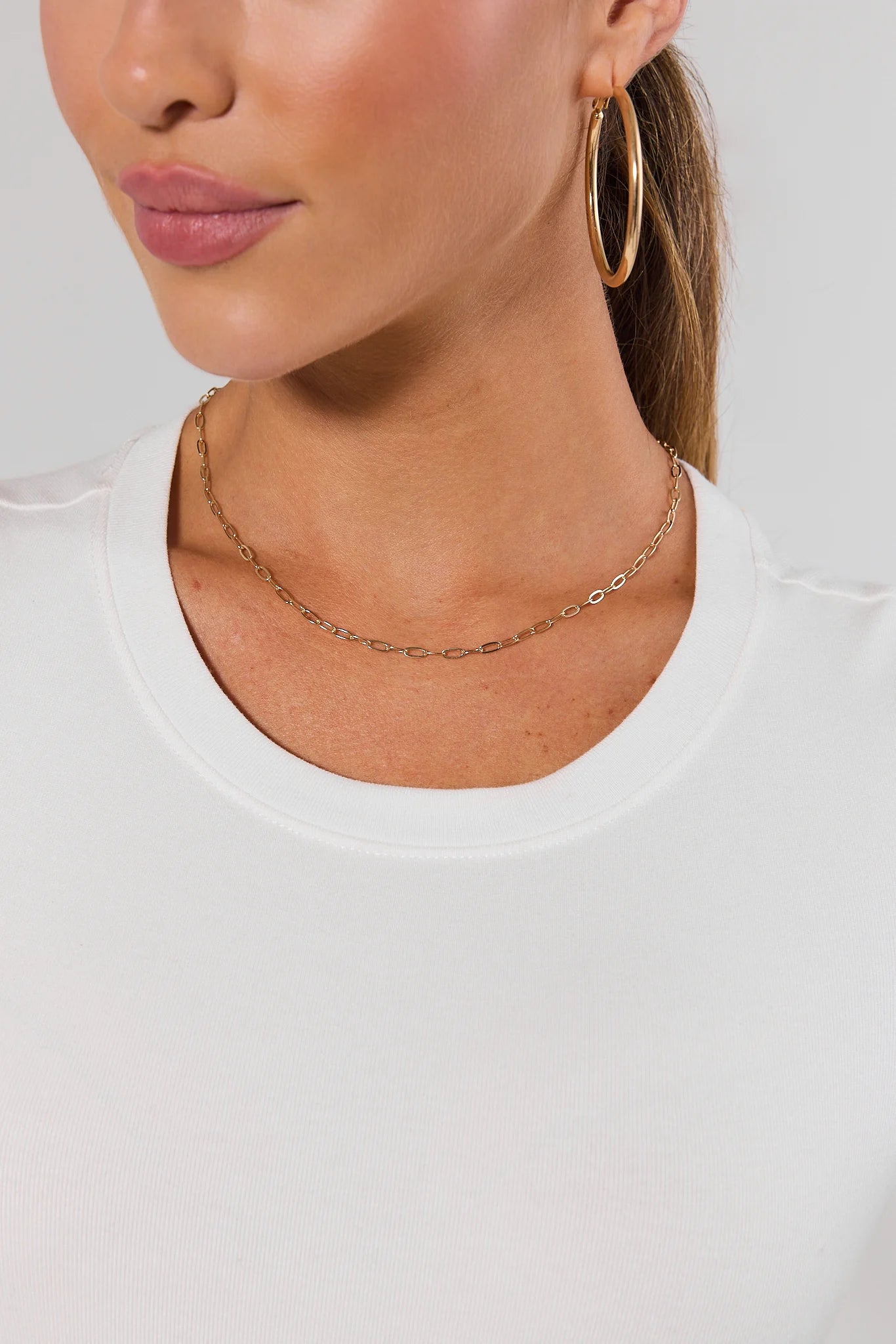 woman wearing A delicate gold chain necklace with a small oval charm and an adjustable lobster clasp, displayed on a clean white background.