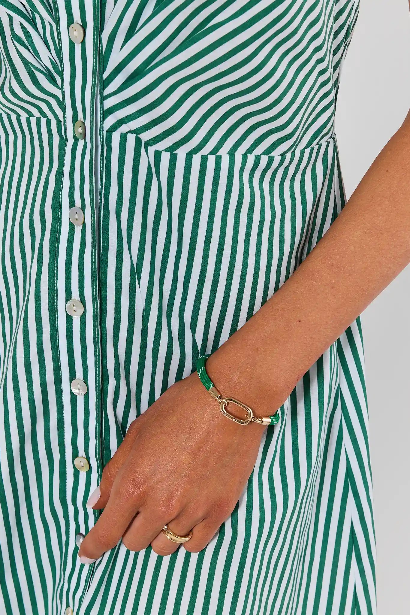 Close-up of a person wearing a green and white vertically striped button-front dress or tunic, with a green bracelet and gold ring on the hand.