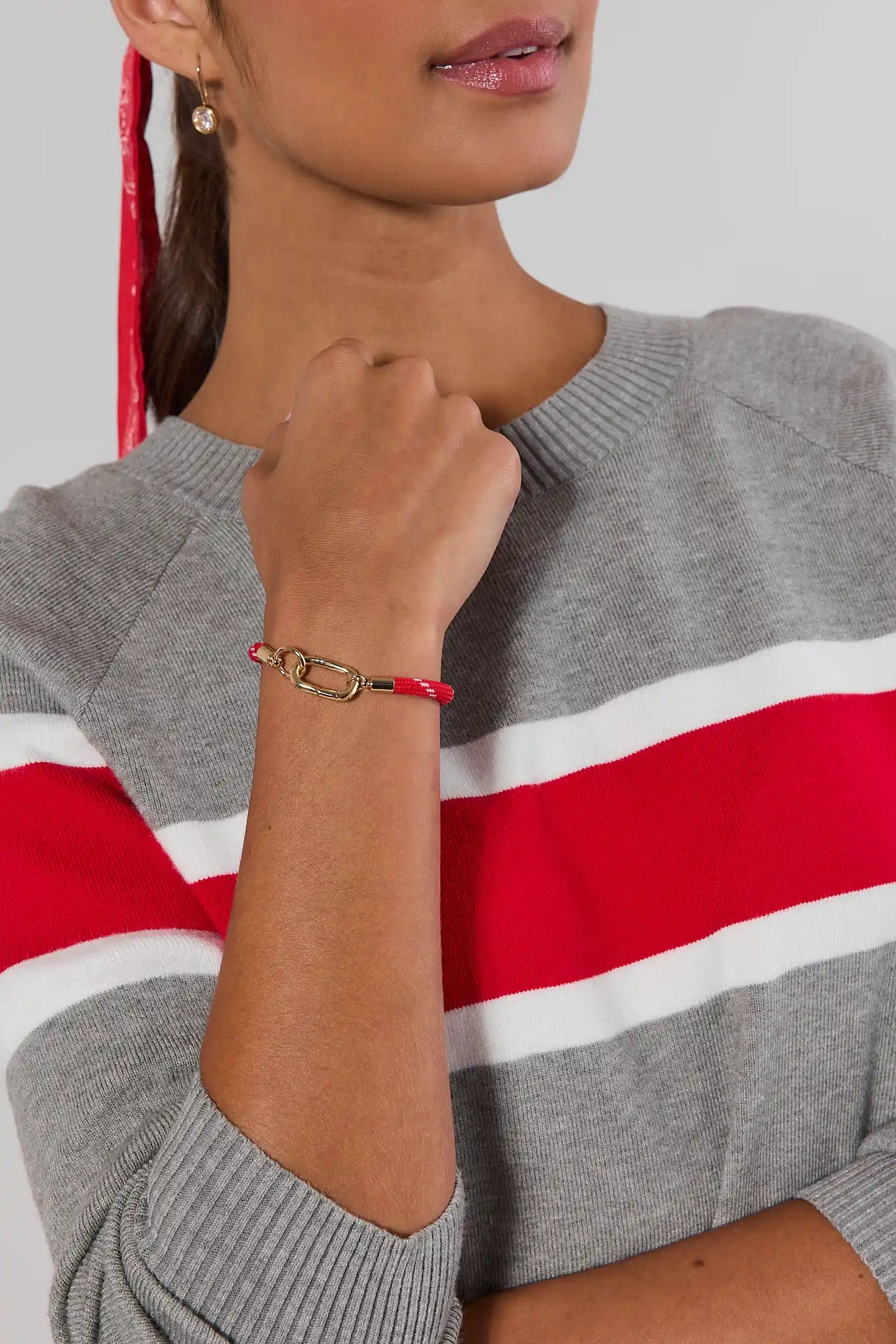 A woman wearing red woven rope bracelet with a gold-tone lobster clasp, displayed on a neutral light gray background.