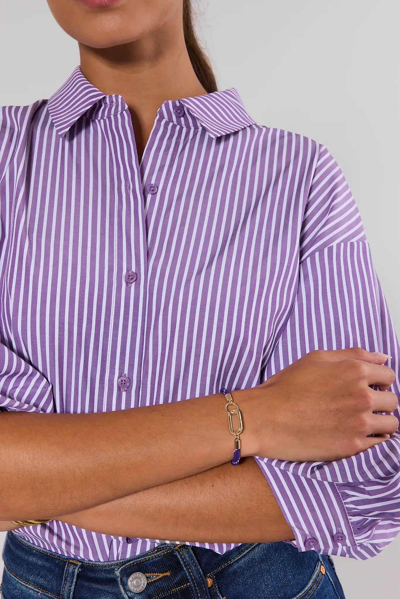 Woman wearing A purple woven rope bracelet with a gold-tone lobster clasp, displayed on a neutral light gray background.