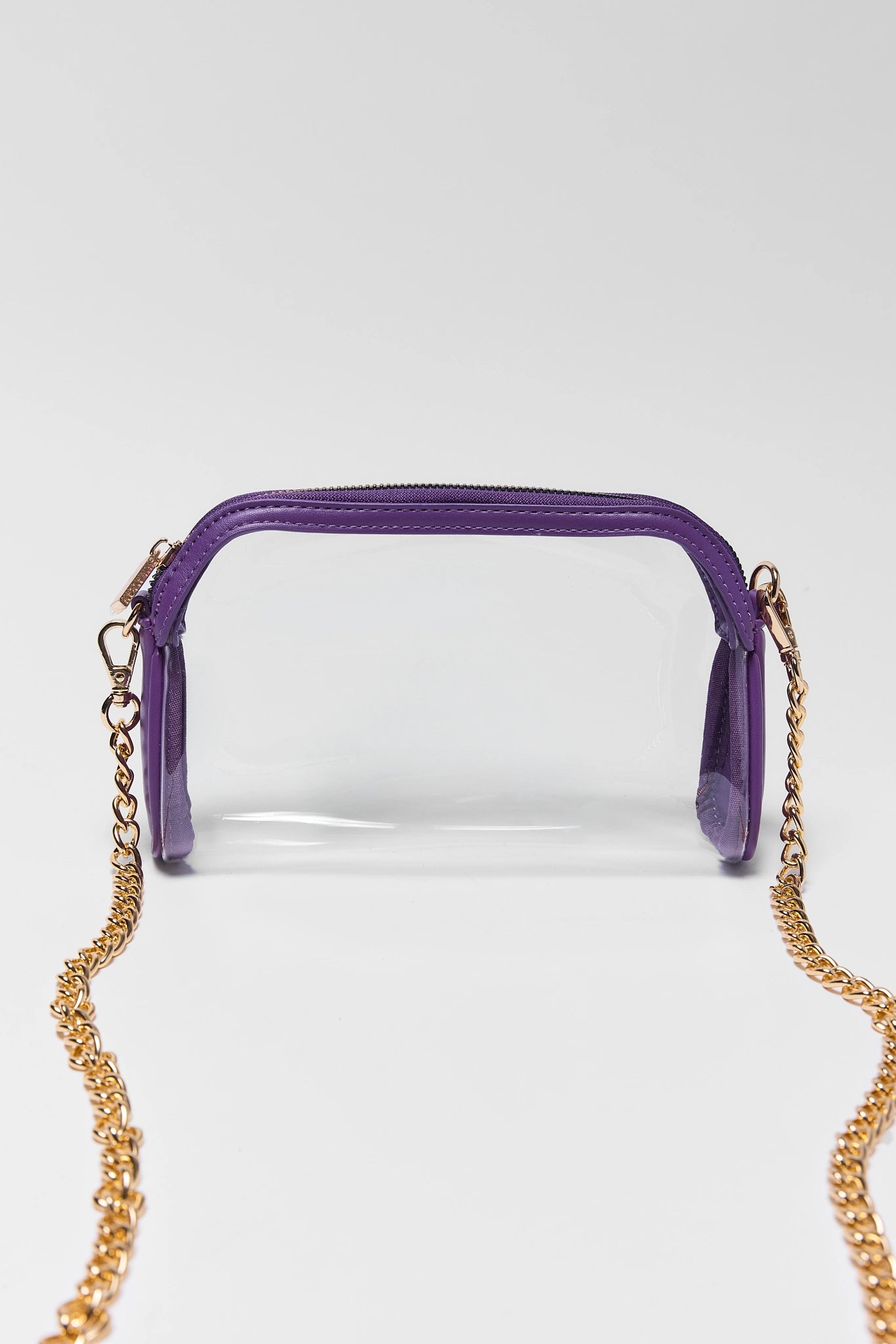 A clear plastic cosmetic pouch with a purple zipper and trim, featuring a gold-tone chain strap, shown against a light gray background.