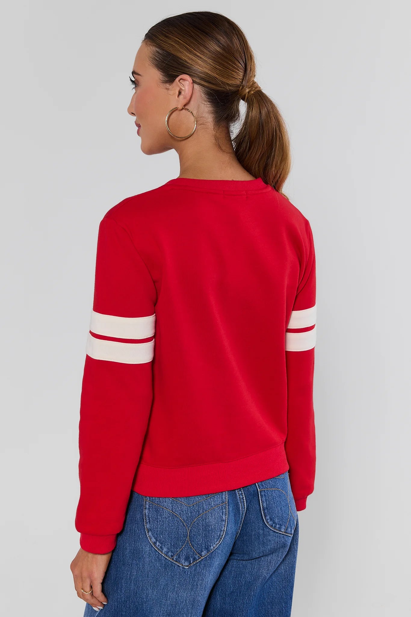 Woman standing wearing Red Varsity Number Pullover with jeans on a white background