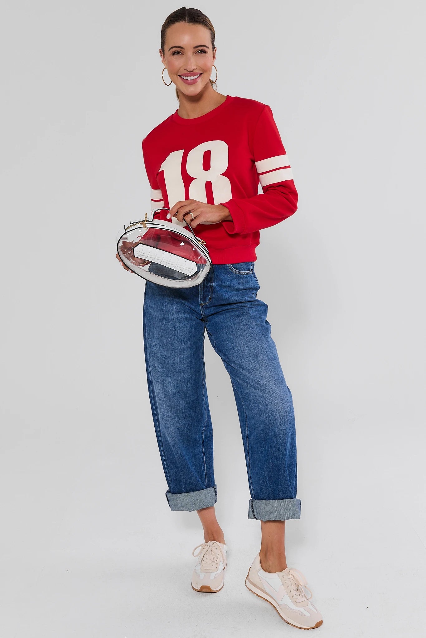 Woman wearing Red Varsity Number Pullover and jeans with football bag on a white background
