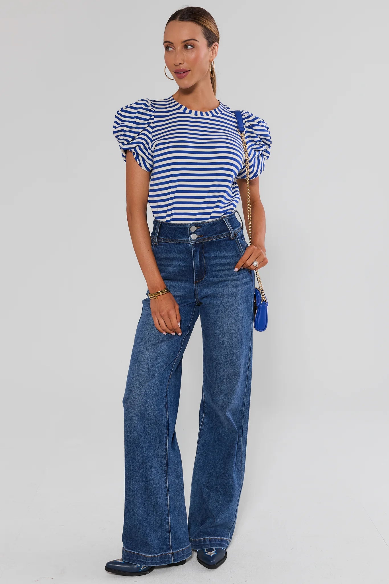 A woman modeling a blue and white striped short-sleeve top with puffed sleeves, paired with high-waisted wide-leg blue jeans, against a light studio background.