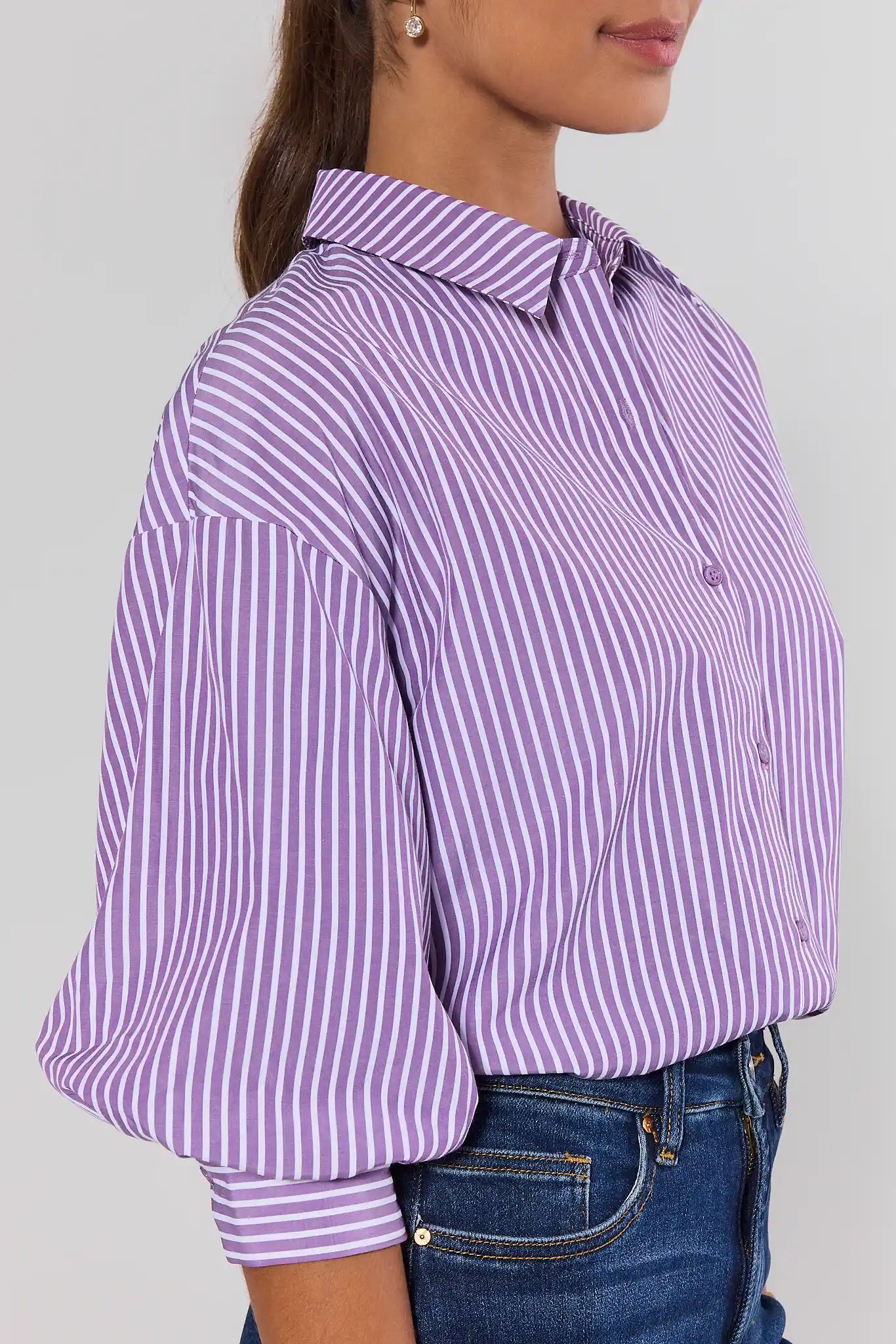 A woman wearing a lavender and white vertically striped button-down shirt with three-quarter sleeves, against a light gray background.