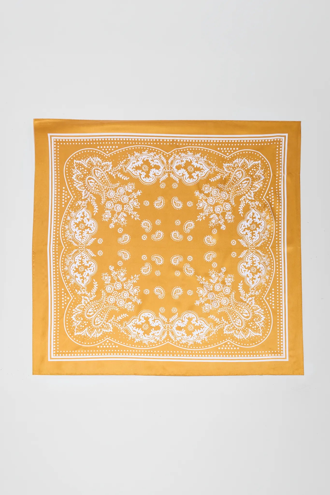 A square yellow bandana with a white paisley and floral border pattern, laid flat against a light gray background.