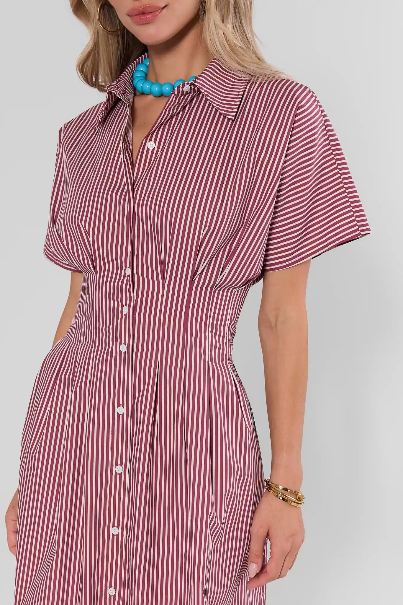 A woman wearing a short-sleeve collared button-front dress with vertical red and white stripes, shown against a light gray studio background.