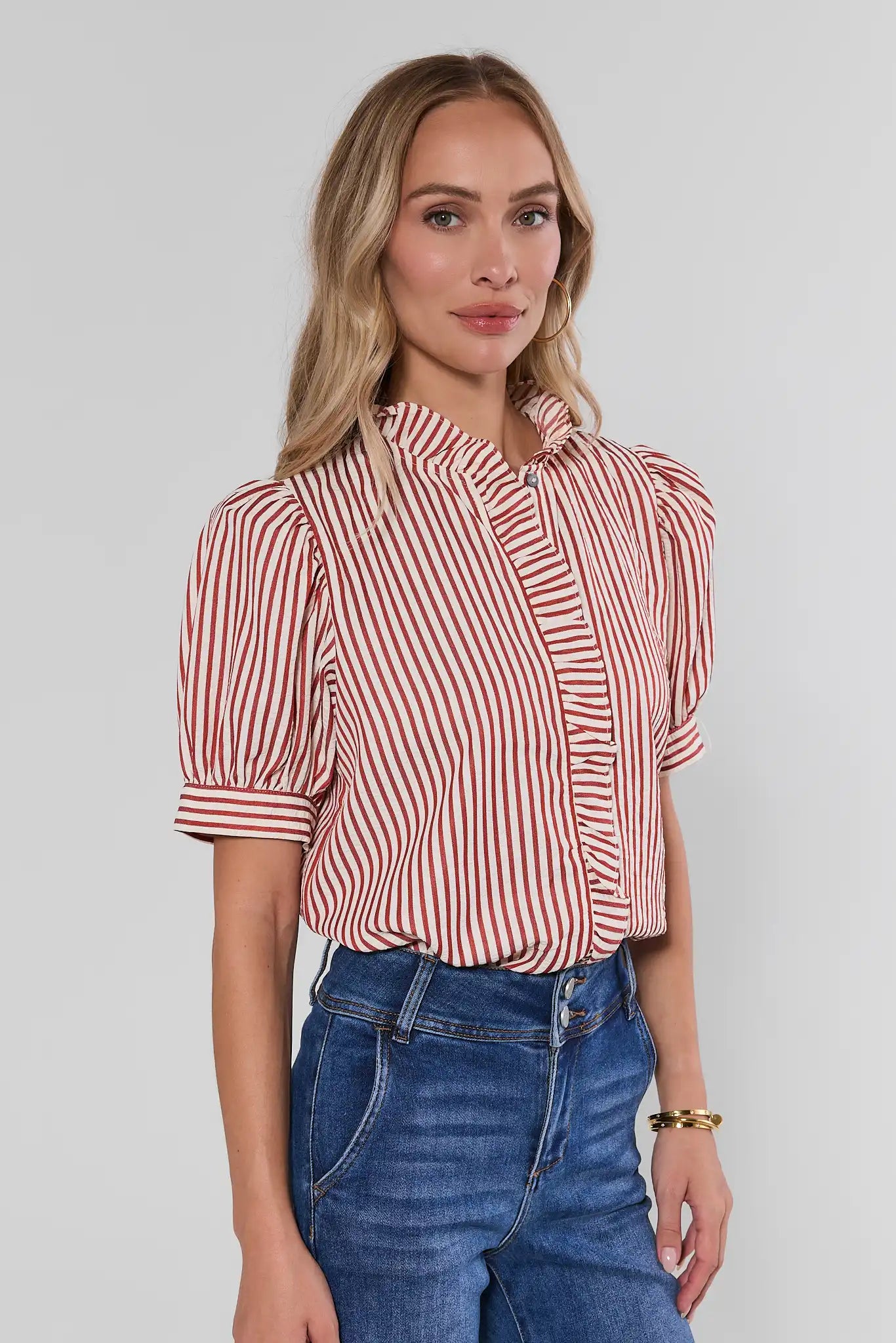 A woman modeling a short-sleeve blouse with vertical red and white stripes, paired with blue jeans, against a light studio background.