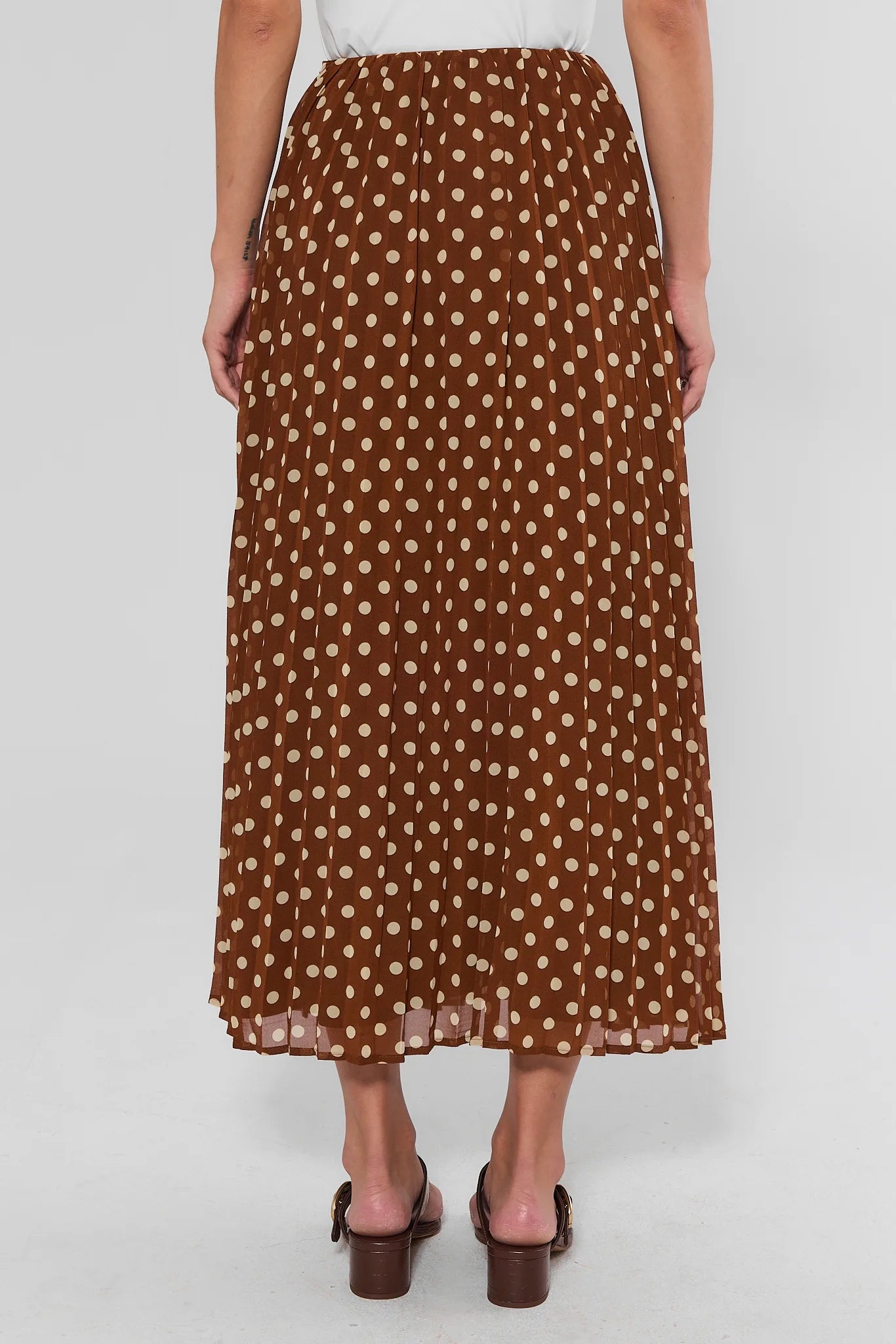 A brown midi skirt with a beige polka dot pattern, shown on a model from the back against a light gray background.