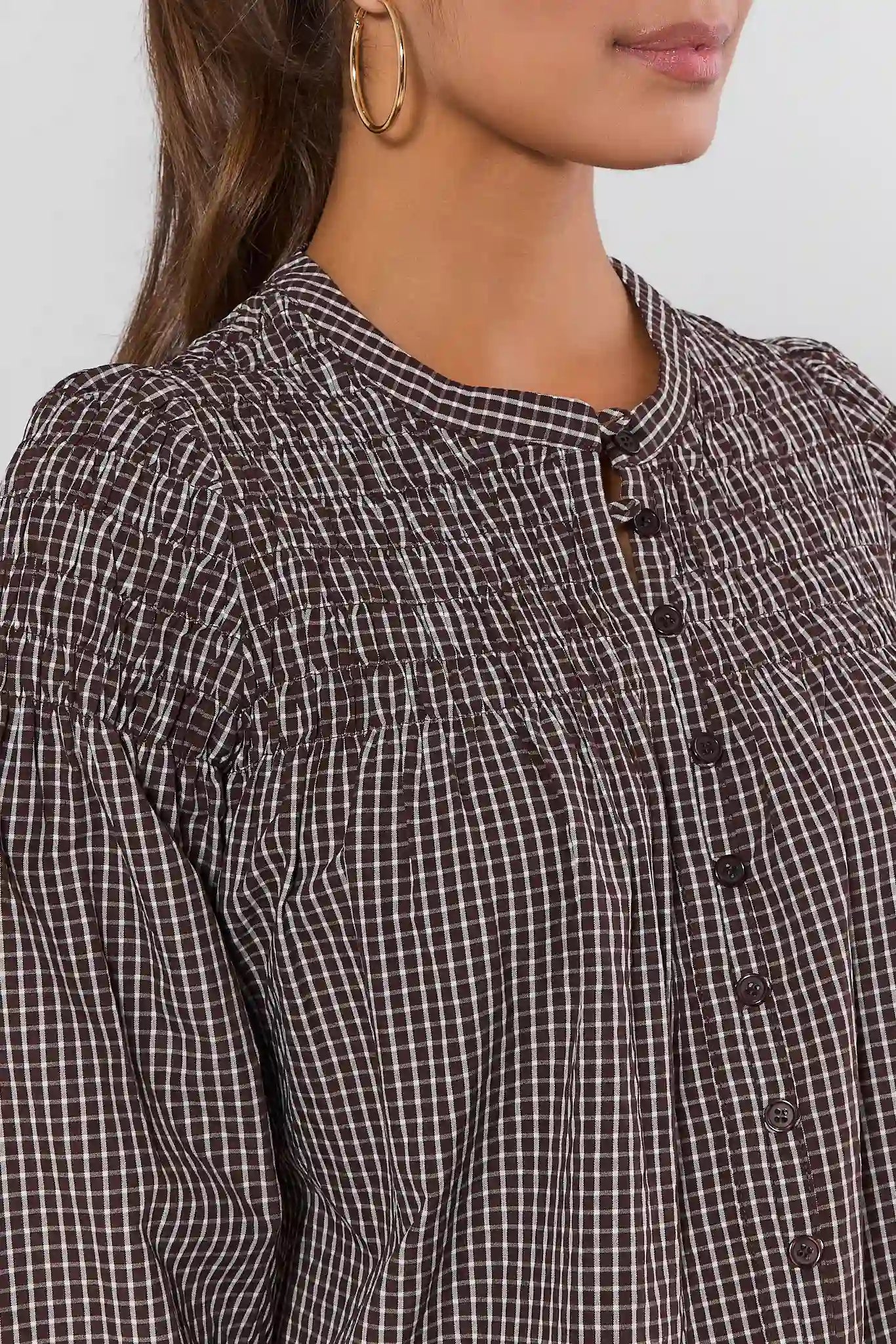 Close-up of a woman wearing a dark brown and white checkered blouse with a smocked bodice and button front.