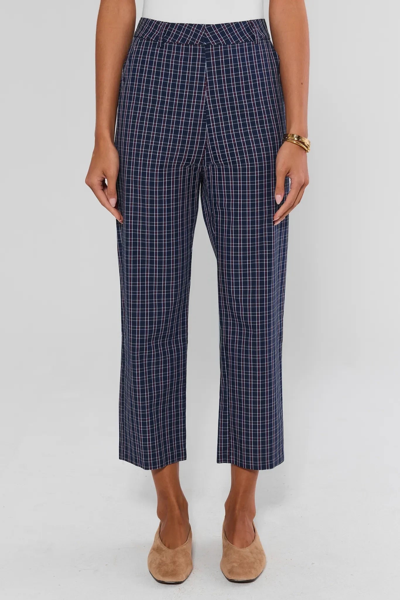 A model is shown from the waist down wearing navy blue cropped trousers with a white and thin red windowpane plaid pattern, paired with beige flat shoes against a light gray background.