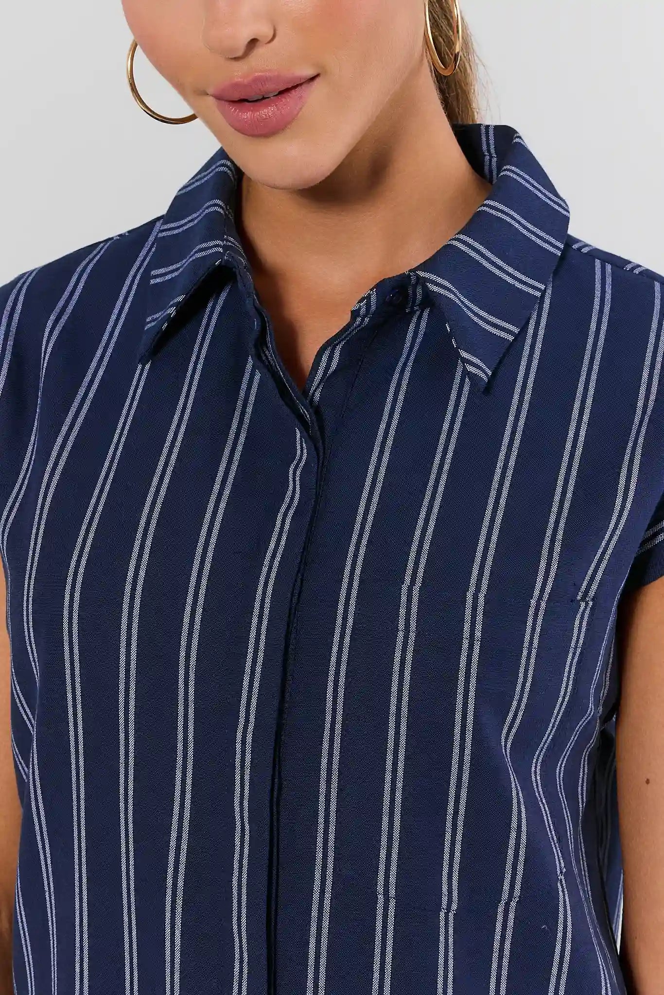 A close-up of a woman wearing a navy blue short-sleeve button-up shirt with thin white vertical pinstripes and a pointed collar.