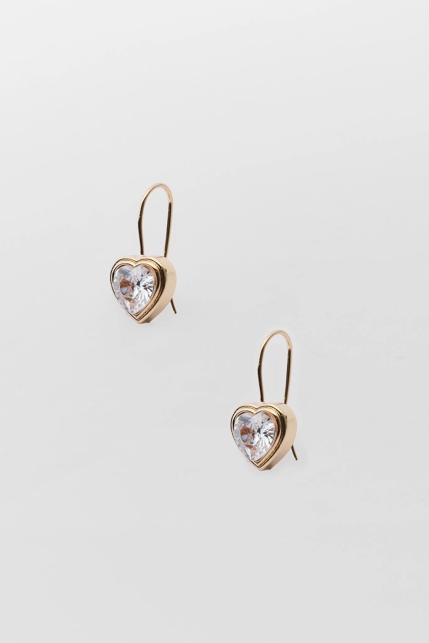 A pair of gold heart-shaped drop earrings with clear heart-shaped crystals, displayed on a light gray background.