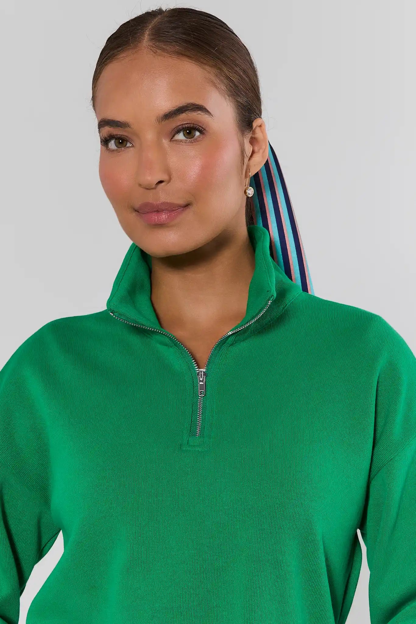 A woman wearing a bright green ribbed quarter-zip pullover sweater, shown from the chest up against a light gray studio background.
