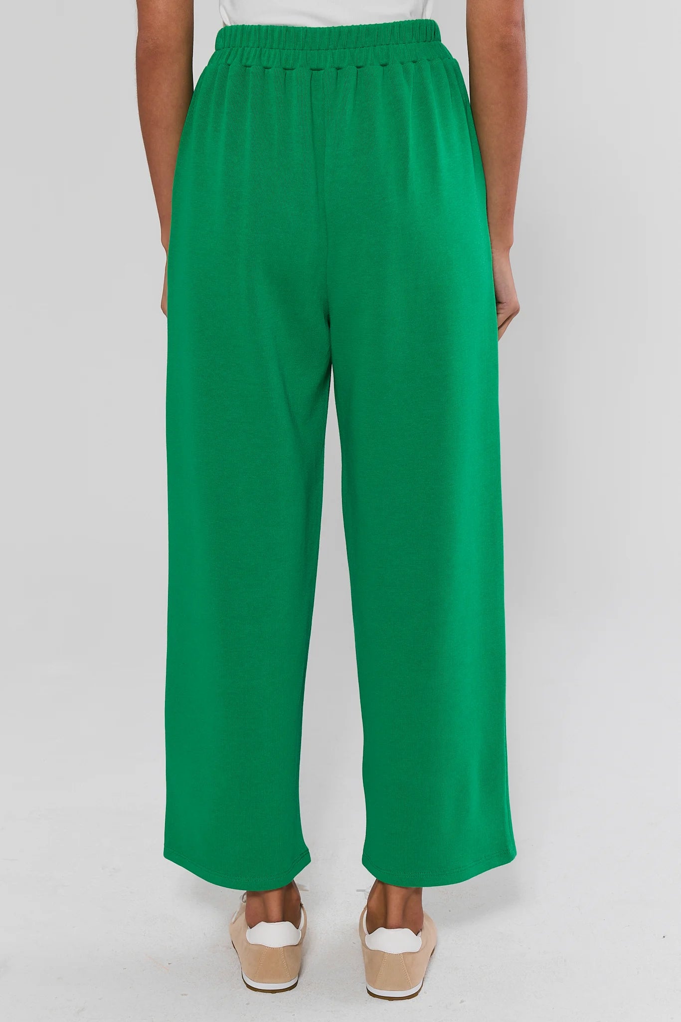 A person shown from the back wearing bright green wide-leg cropped pants with an elastic waistband, paired with beige wedge sandals against a light gray studio background.
