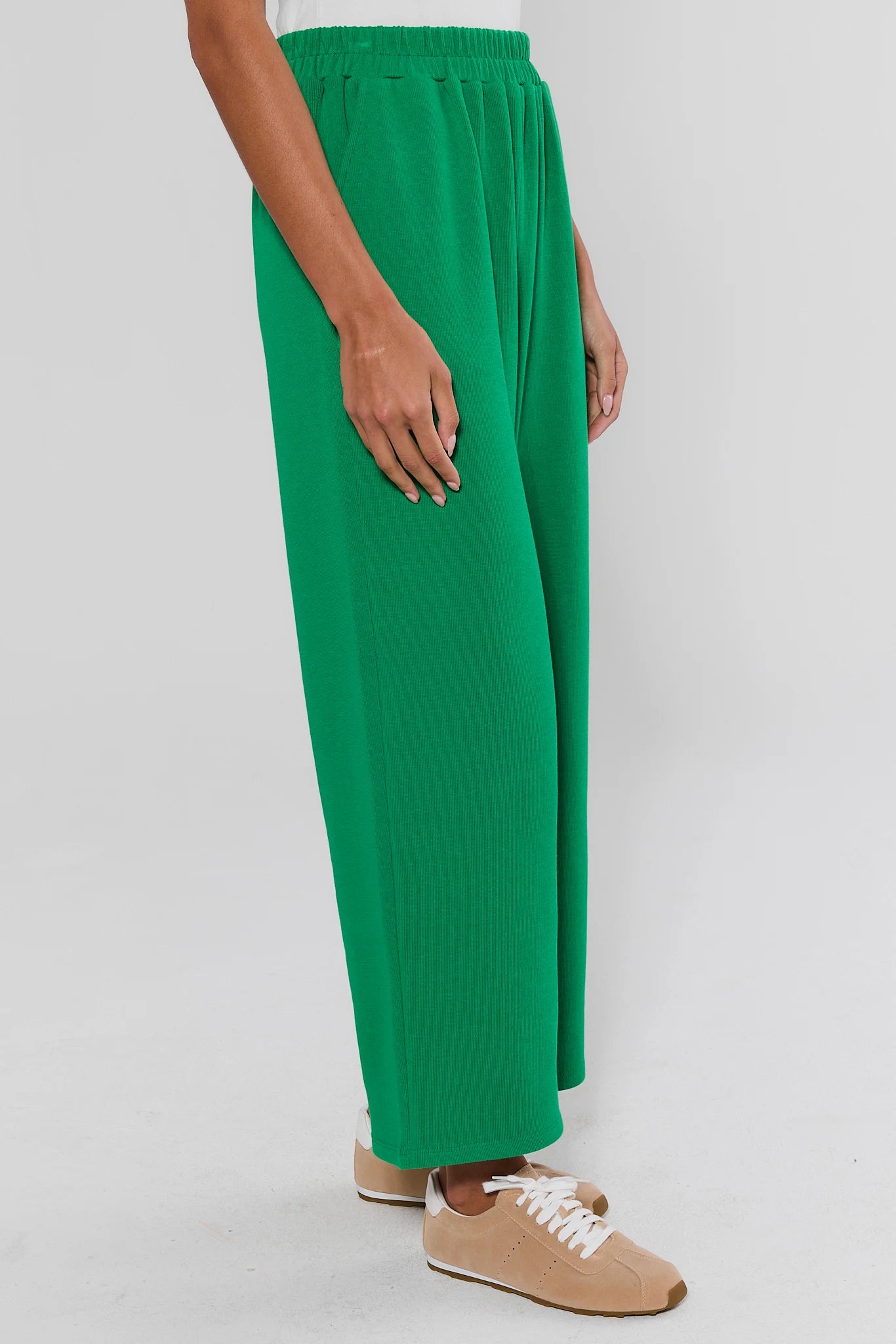 A person wearing bright green wide-leg knit pants with an elastic waistband, paired with beige sneakers, shown against a light gray studio background.