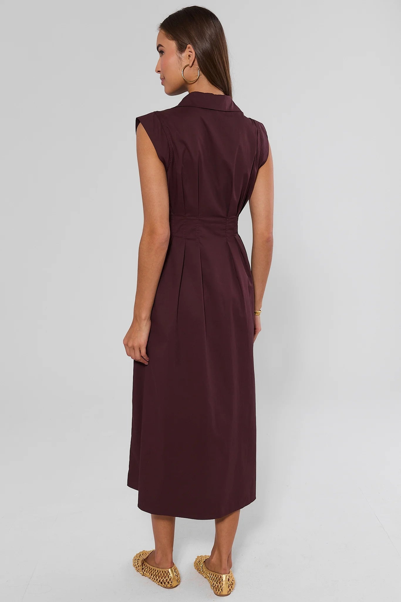 A woman modeling a sleeveless, collared midi dress in a deep burgundy color, shown from the back against a light gray studio background.
