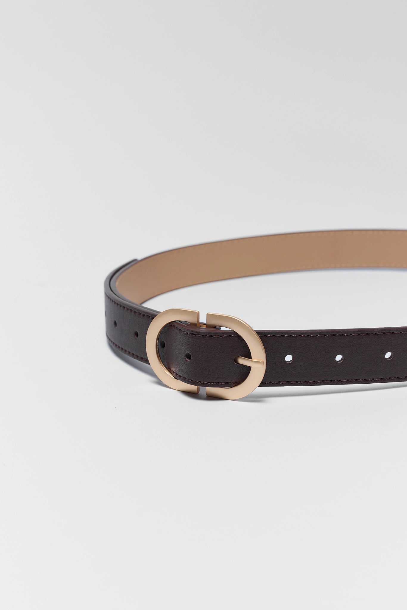 A dark brown leather belt with a light tan interior and a gold-tone oval buckle, shown on a light gray background.