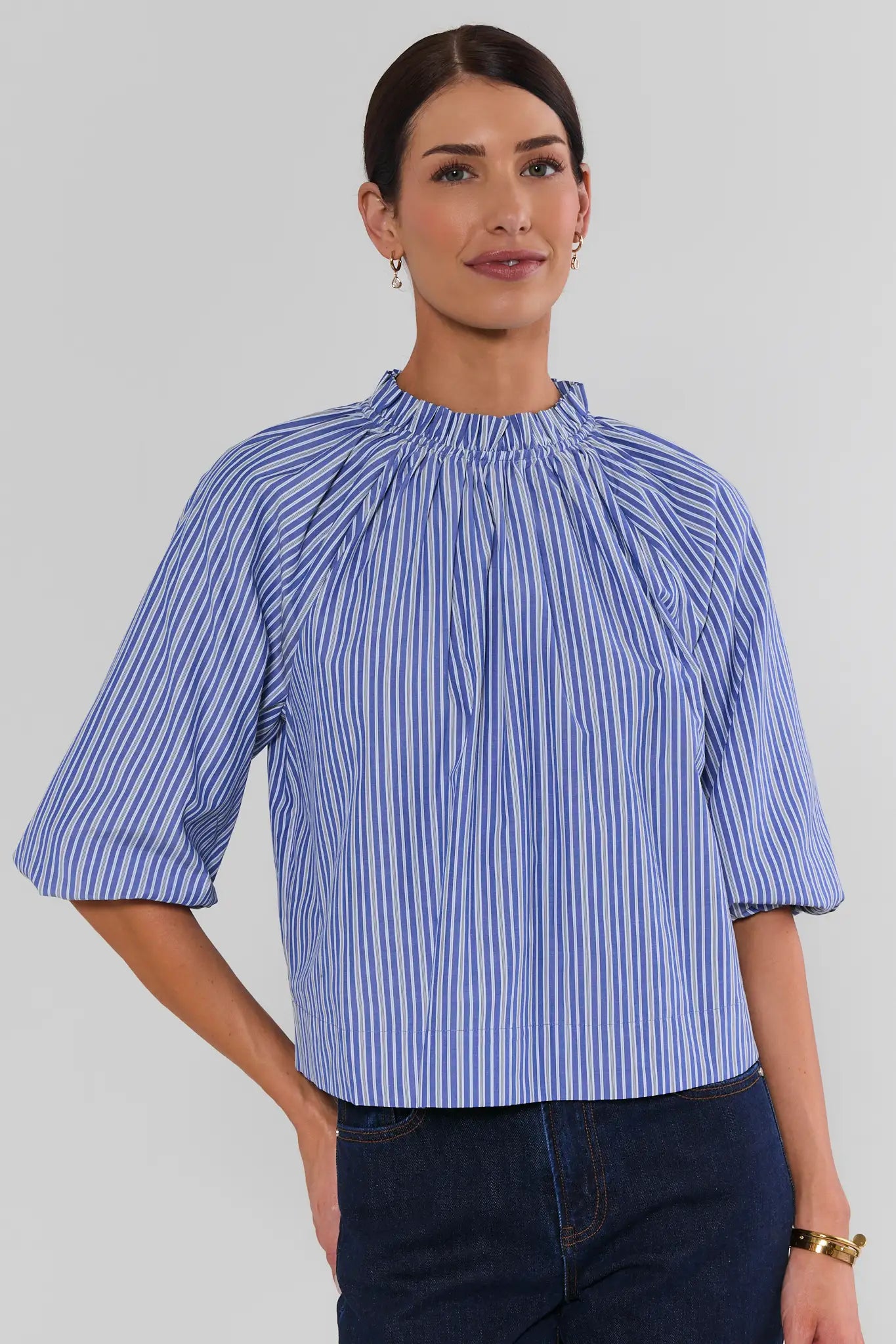 Blue Striped Ruffle Collar Top featuring blue-and-white vertical stripes, a gathered ruffle mock neckline, three-quarter puff sleeves, and a relaxed fit, styled with dark denim jeans.