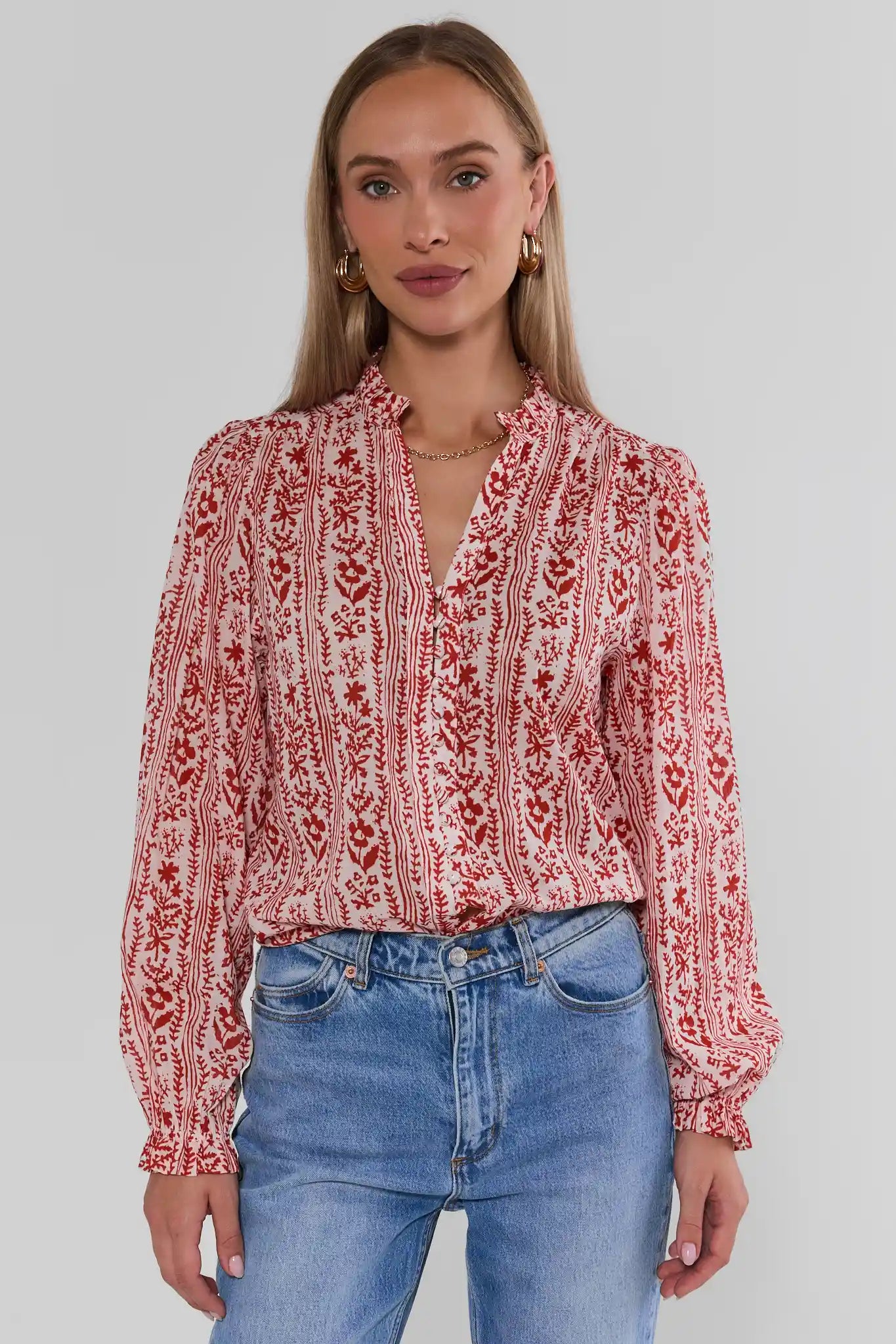 A woman wearing Red Floral Printed Button Up Top paired with blue jeans, against a light gray studio background.