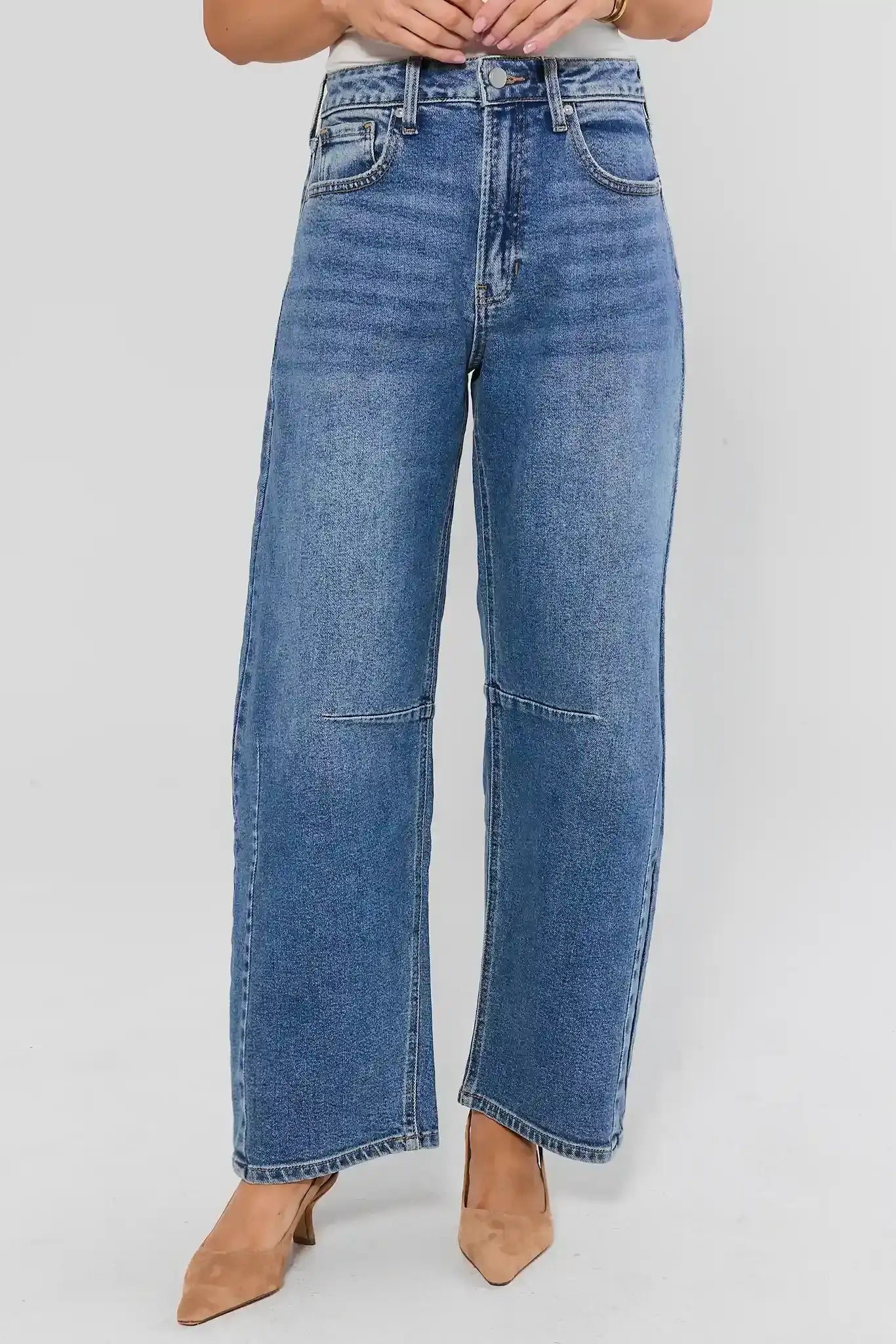 A person wearing high-waisted, wide-leg blue denim jeans with a faded wash and tan pointed-toe heels, shown against a light gray studio background.