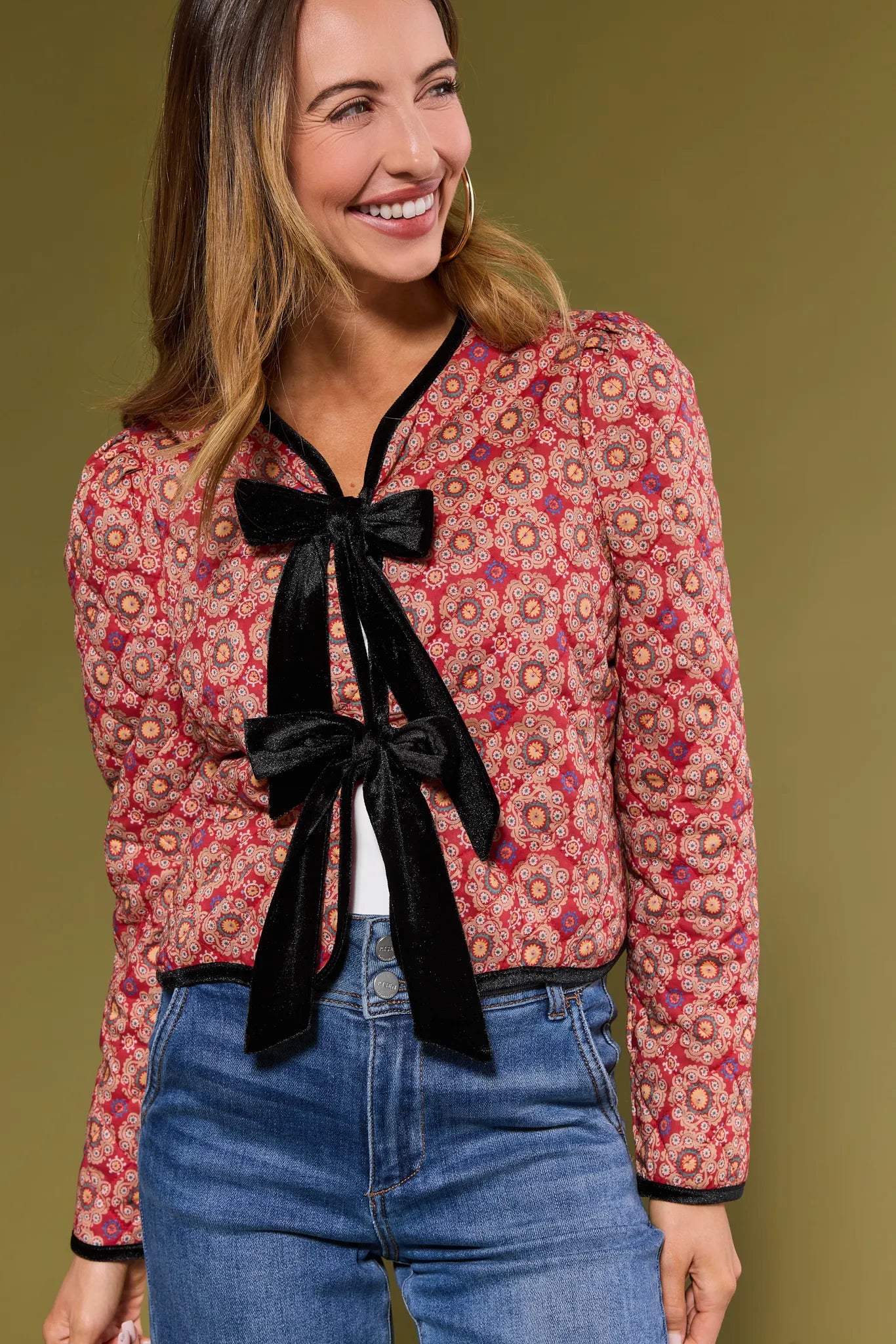 Woman wearing a patterned Ember Jacket with a black bow and jeans on a green background