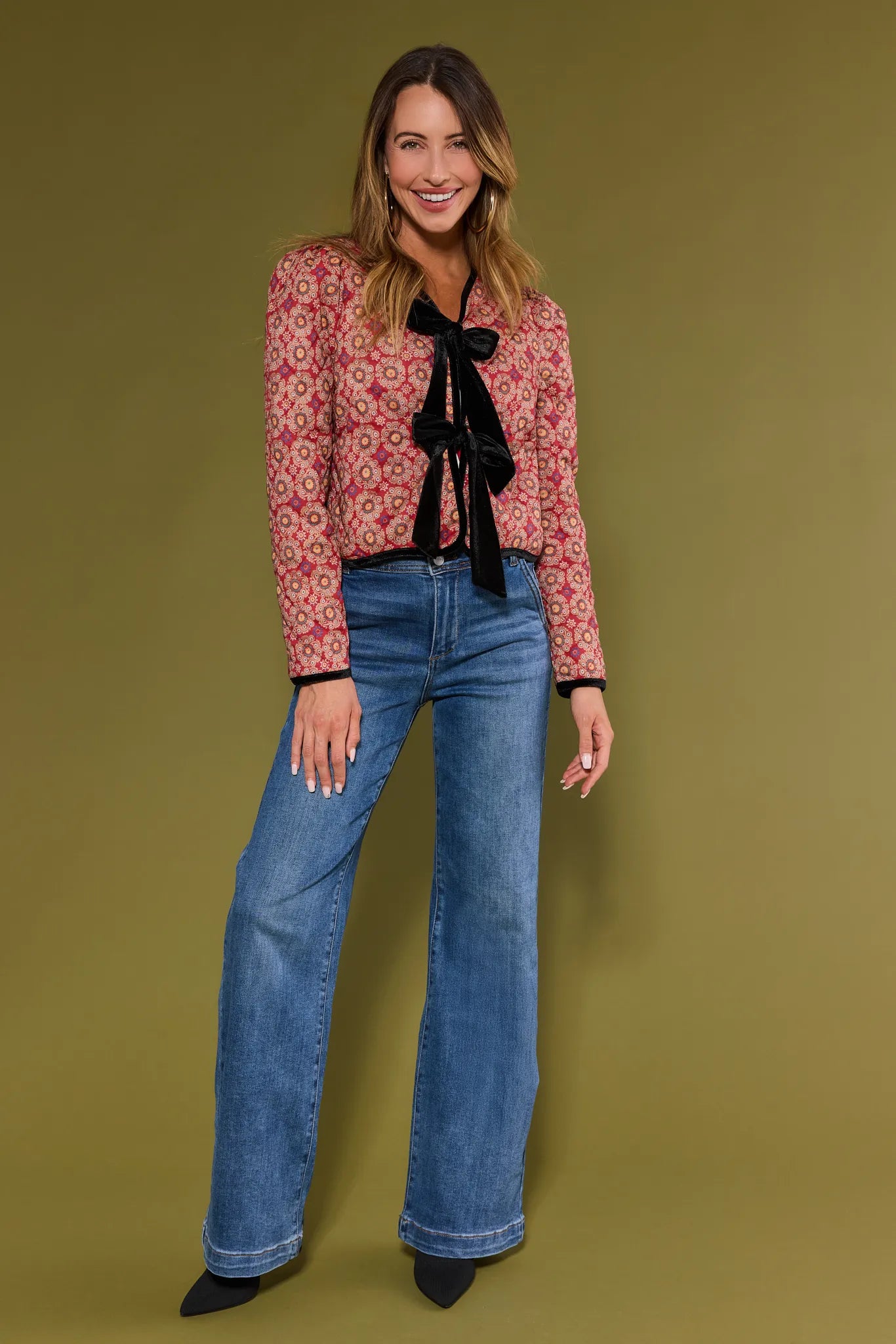 Woman wearing a red floral Ember Jacket with a black tie and blue jeans on a green background